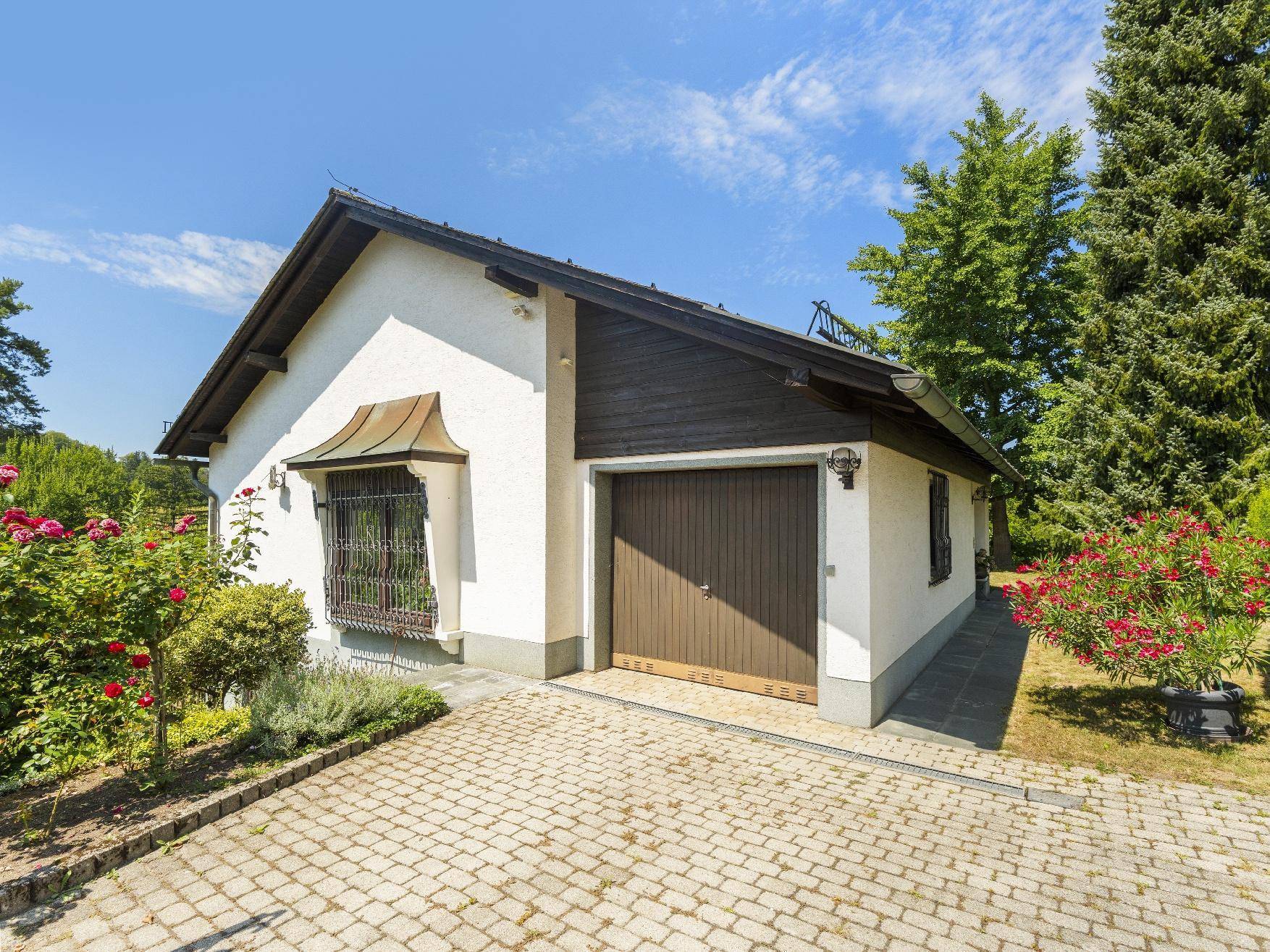 Freistehende Garage mit gepflasterter Zufahrt und gepflegter Bepflanzung im Vorgartenbereich.