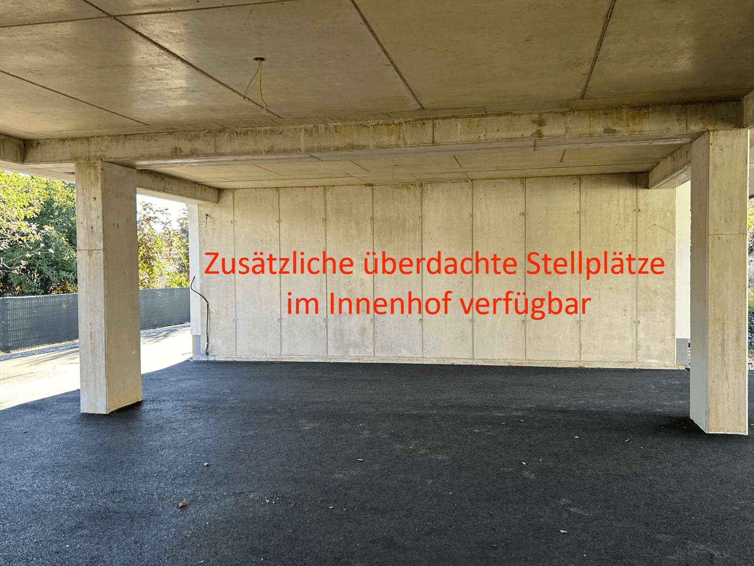 Überdachte Stellplätze im Innenhof mit robusten Betonstützen und einem asphaltierten Bodenbelag.