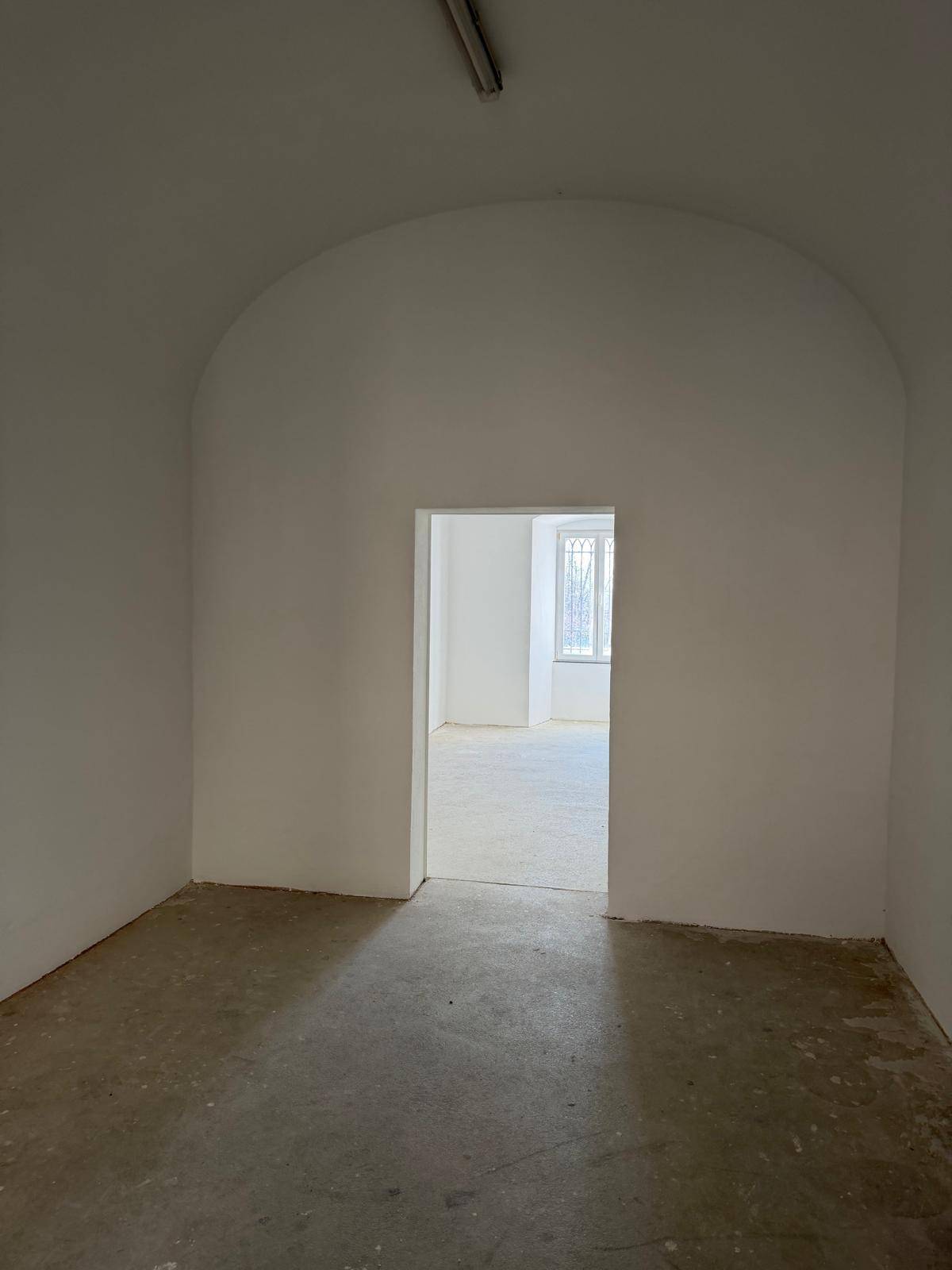 Durchgang zu einem helleren Raum mit Fenster, gekennzeichnet durch eine gewölbte Türöffnung.
