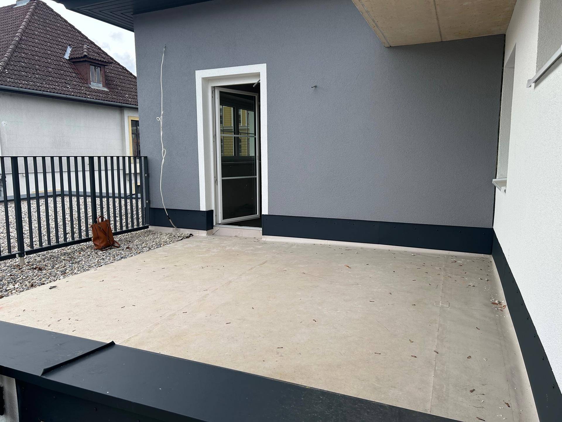 Geräumige, unmöblierte Terrasse mit Betonboden und direktem Zugang zu einem Innenraum des Gebäudes.