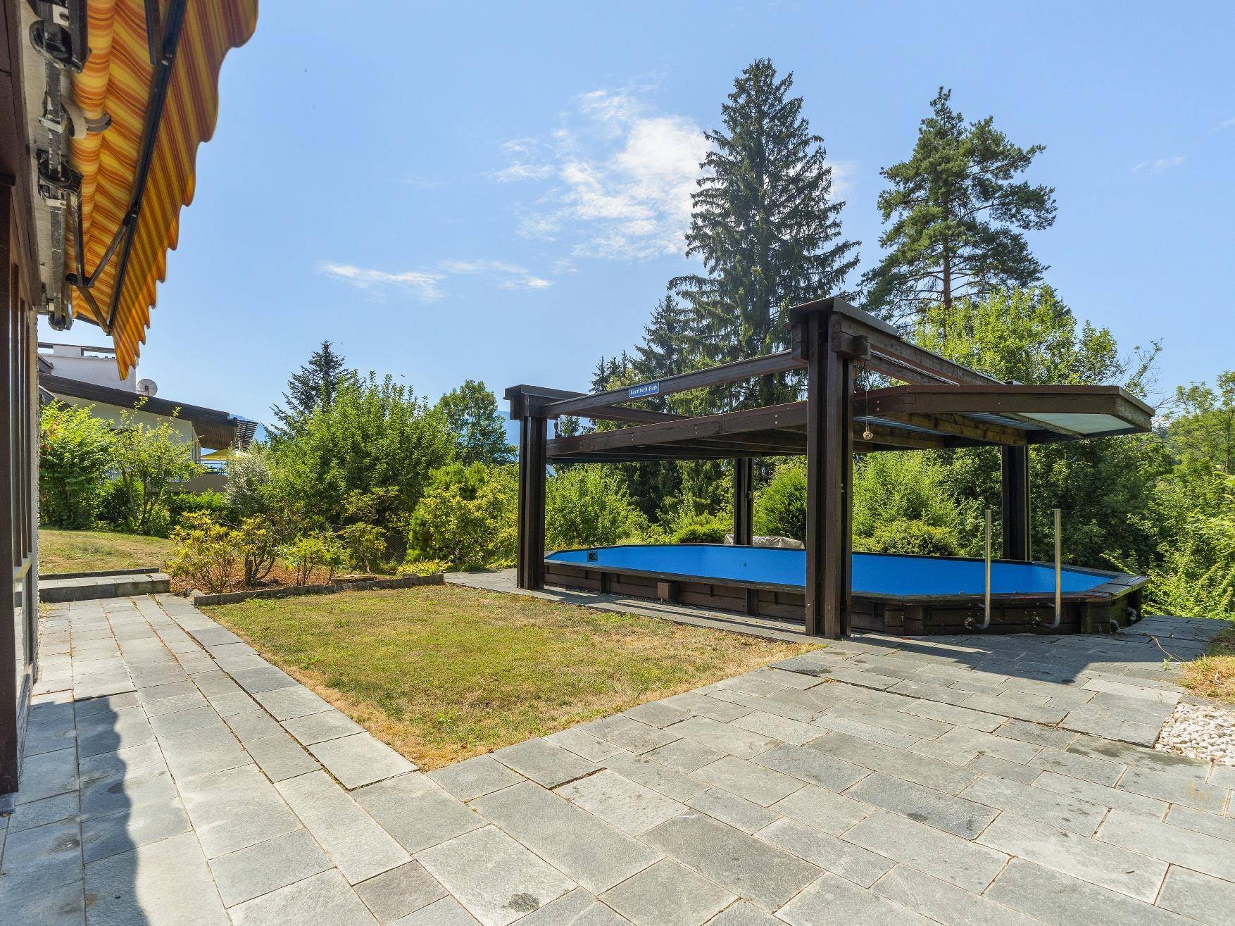 Große gepflasterte Terrasse neben dem Haus mit Blick auf den Pool und die grüne Umgebung.