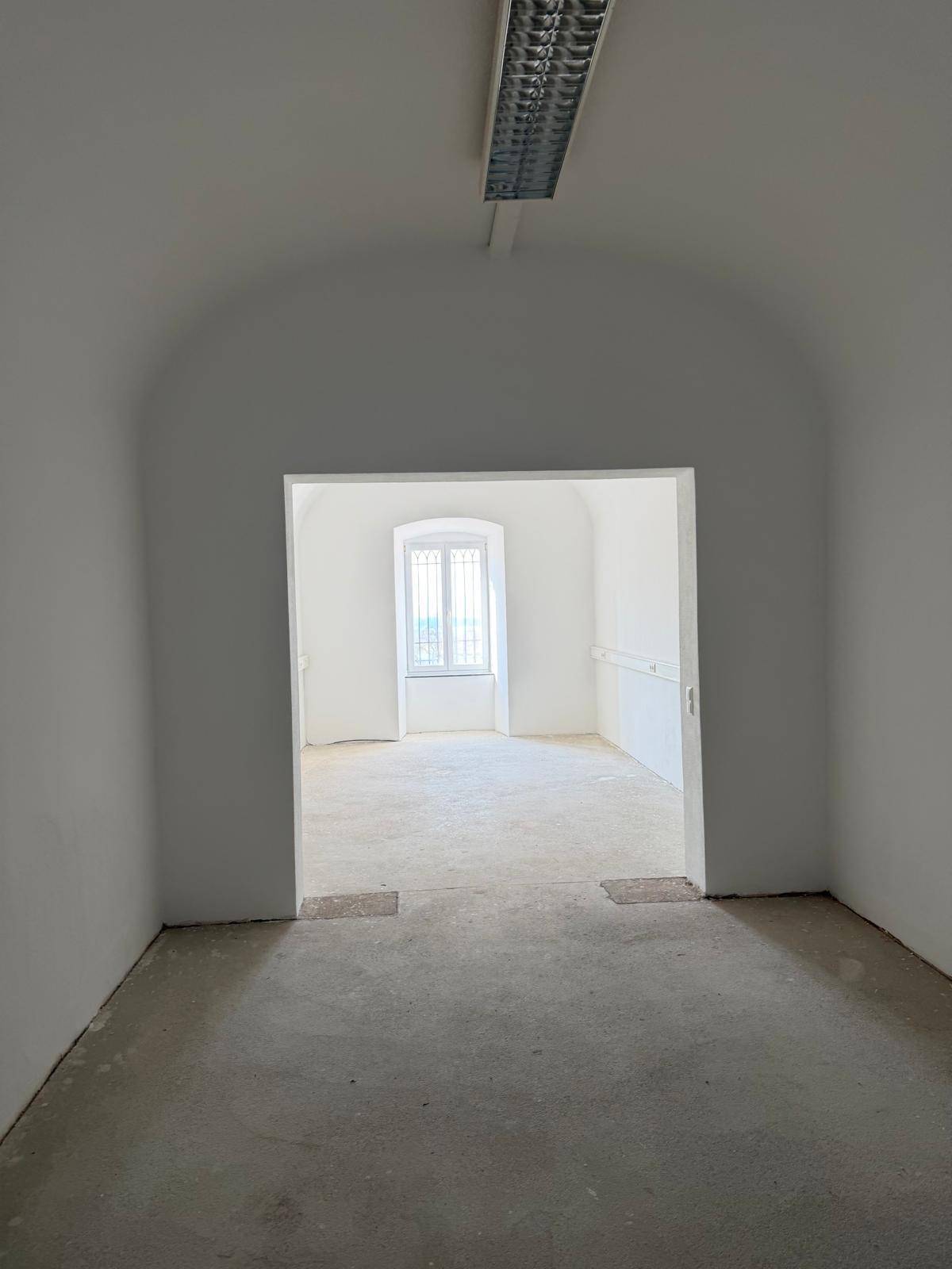 Durchgang zu einem helleren Raum mit Fenster, gekennzeichnet durch eine gewölbte Türöffnung.