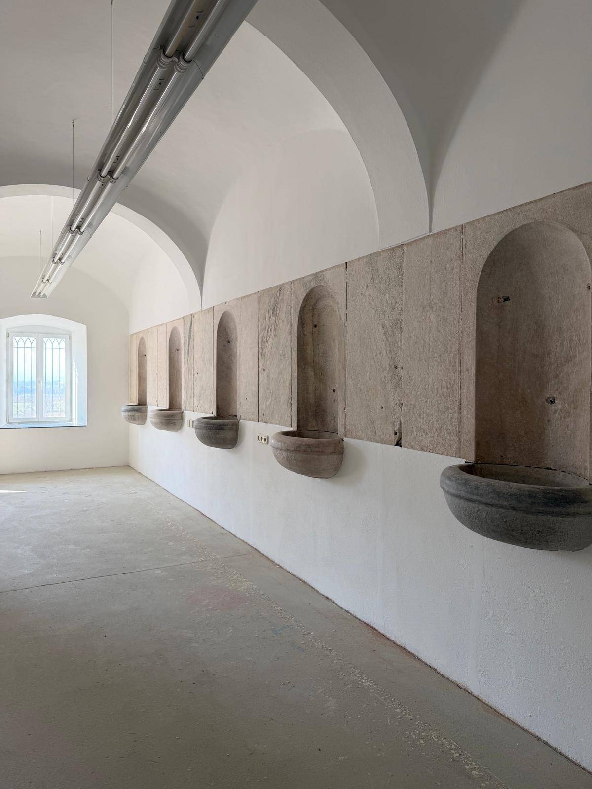 Heller Innenraum mit Gewölbedecke, Steinbecken an der Wand und einem Fenster.