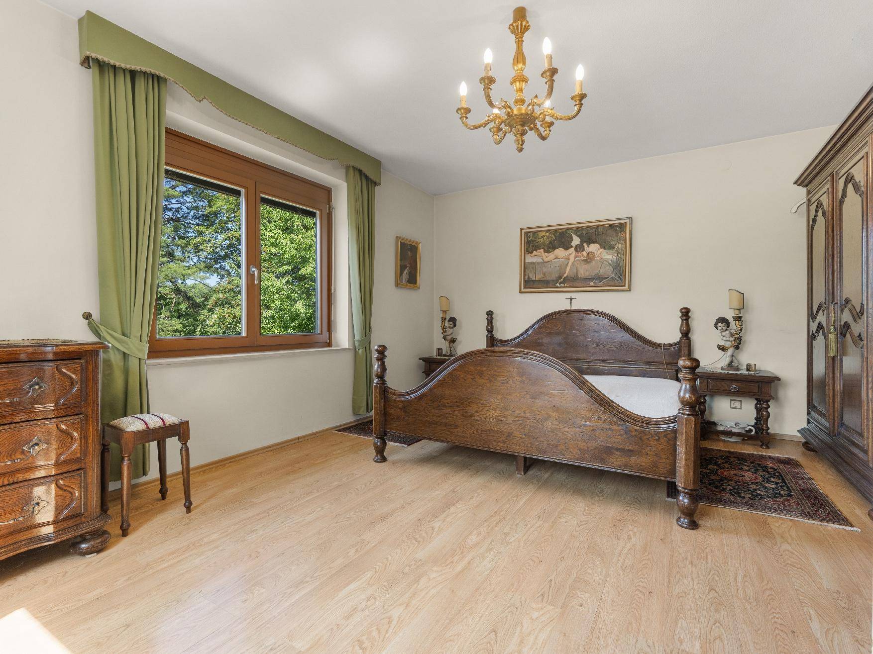 Helles Schlafzimmer mit Holzbett, Laminatboden und Blick ins Grüne.