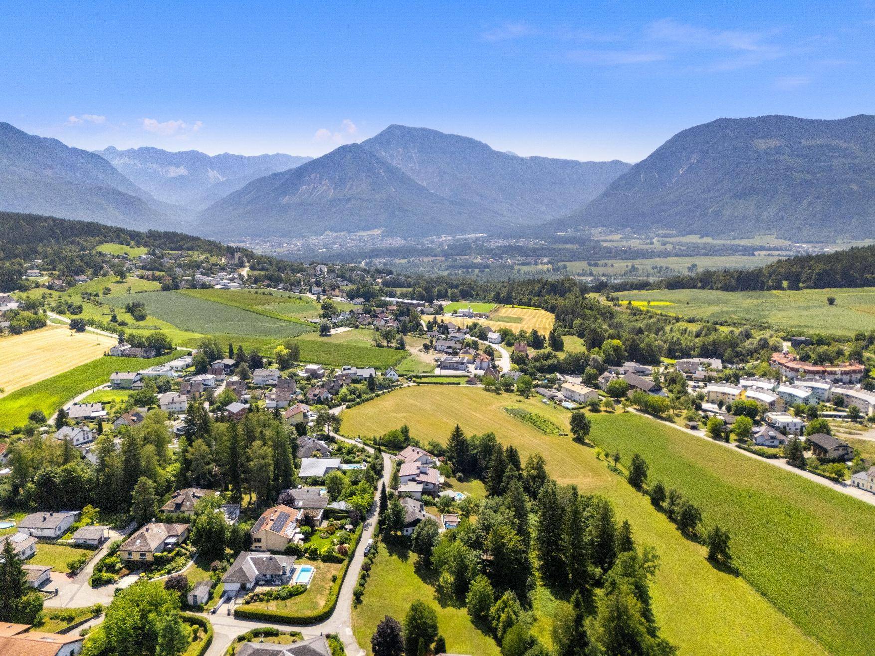 Weitläufige Landschaftsaufnahme mit Wohnsiedlung, Feldern und majestätischen Bergen im Hintergrund.