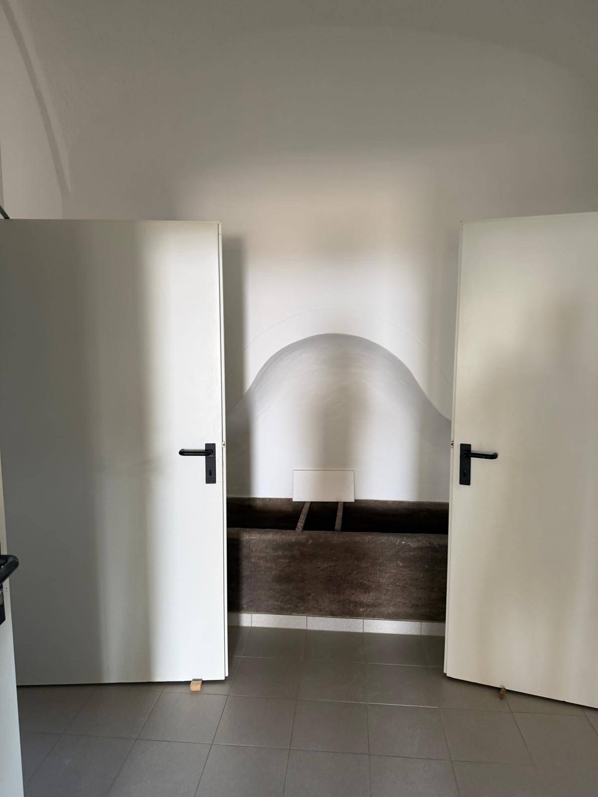 Badezimmerbereich mit zwei Türen, grauen Fliesen und einer Nische in der Wand.