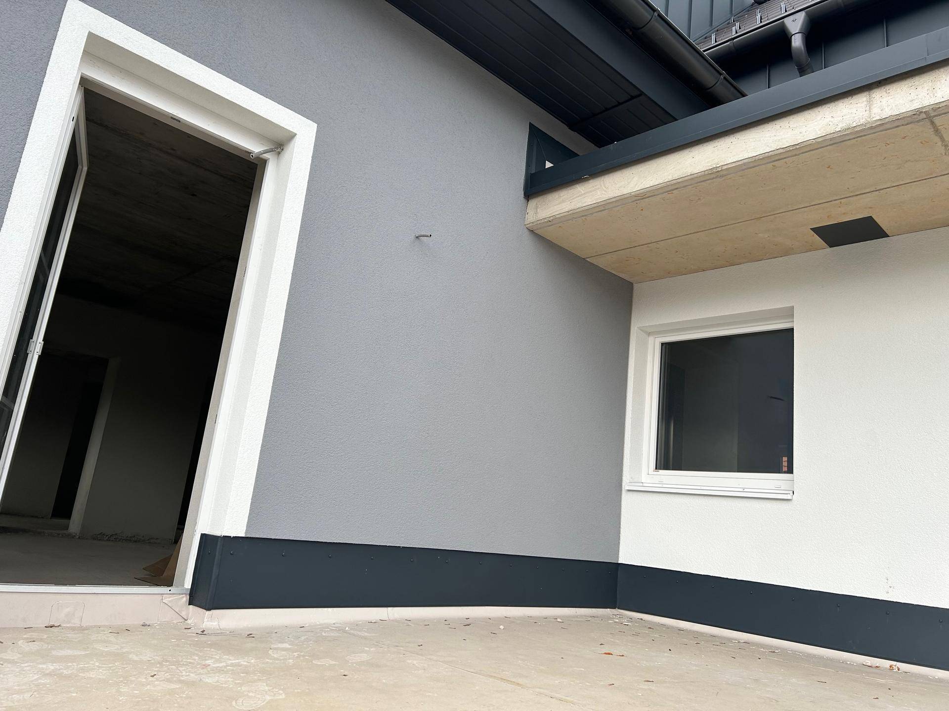 Detailansicht einer Terrasse mit Zugangstür und der modernen grauen Fassade des Neubaus.