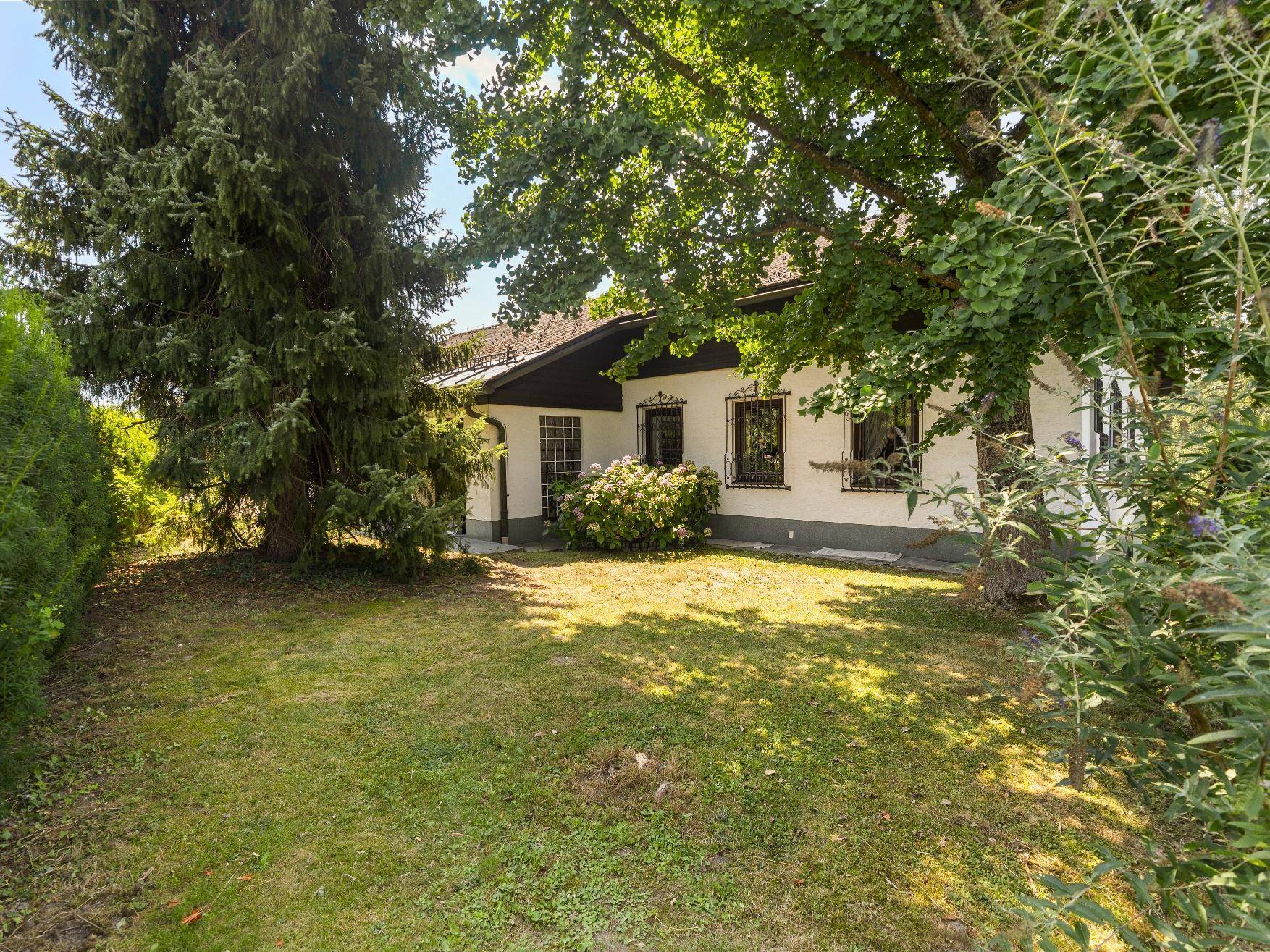 Teilansicht des Hauses mit weitläufigem Rasenbereich und altem Baumbestand im Garten.