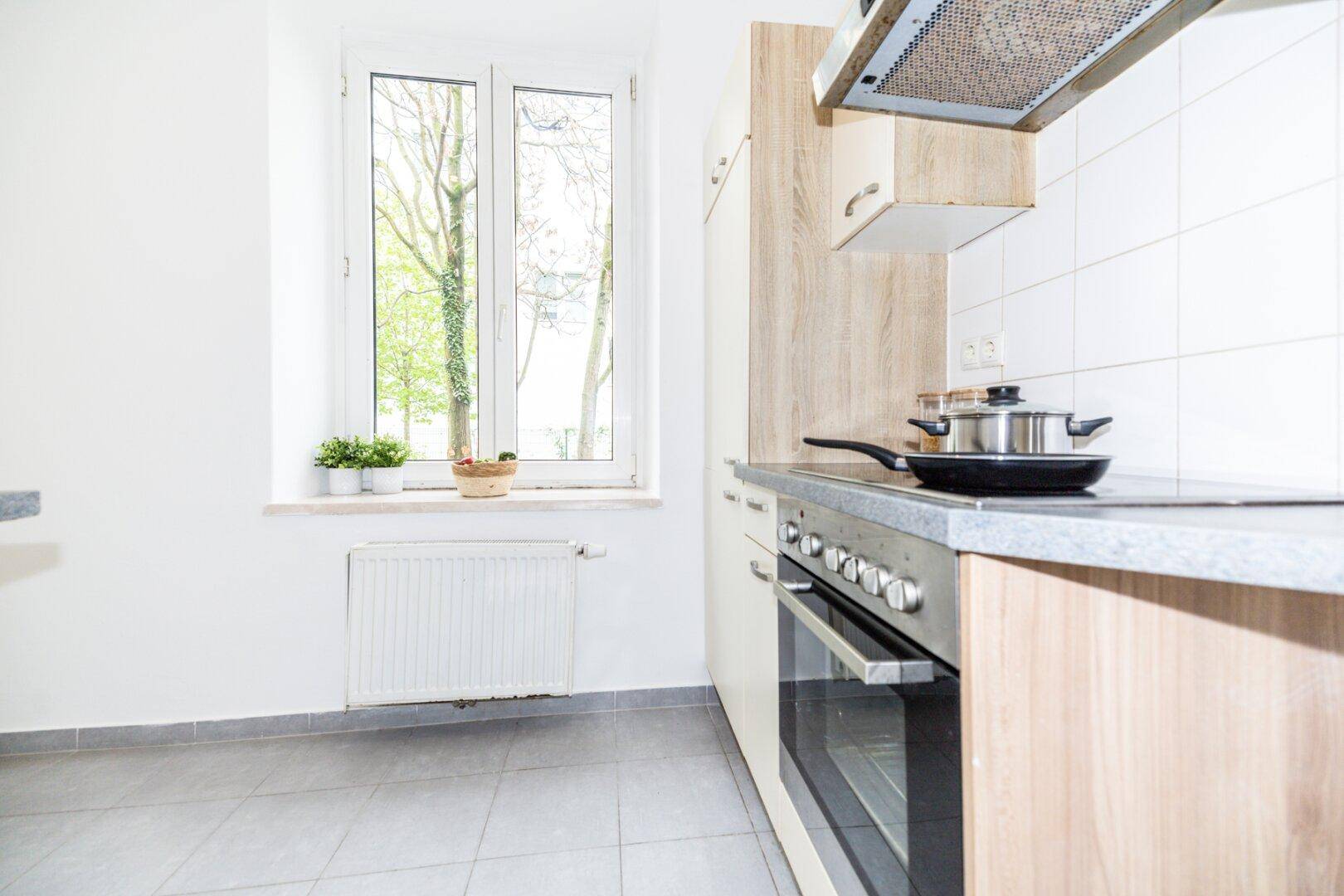 Moderne Küche mit hellen Holz- und weißen Schränken, Herd und Fenster.
