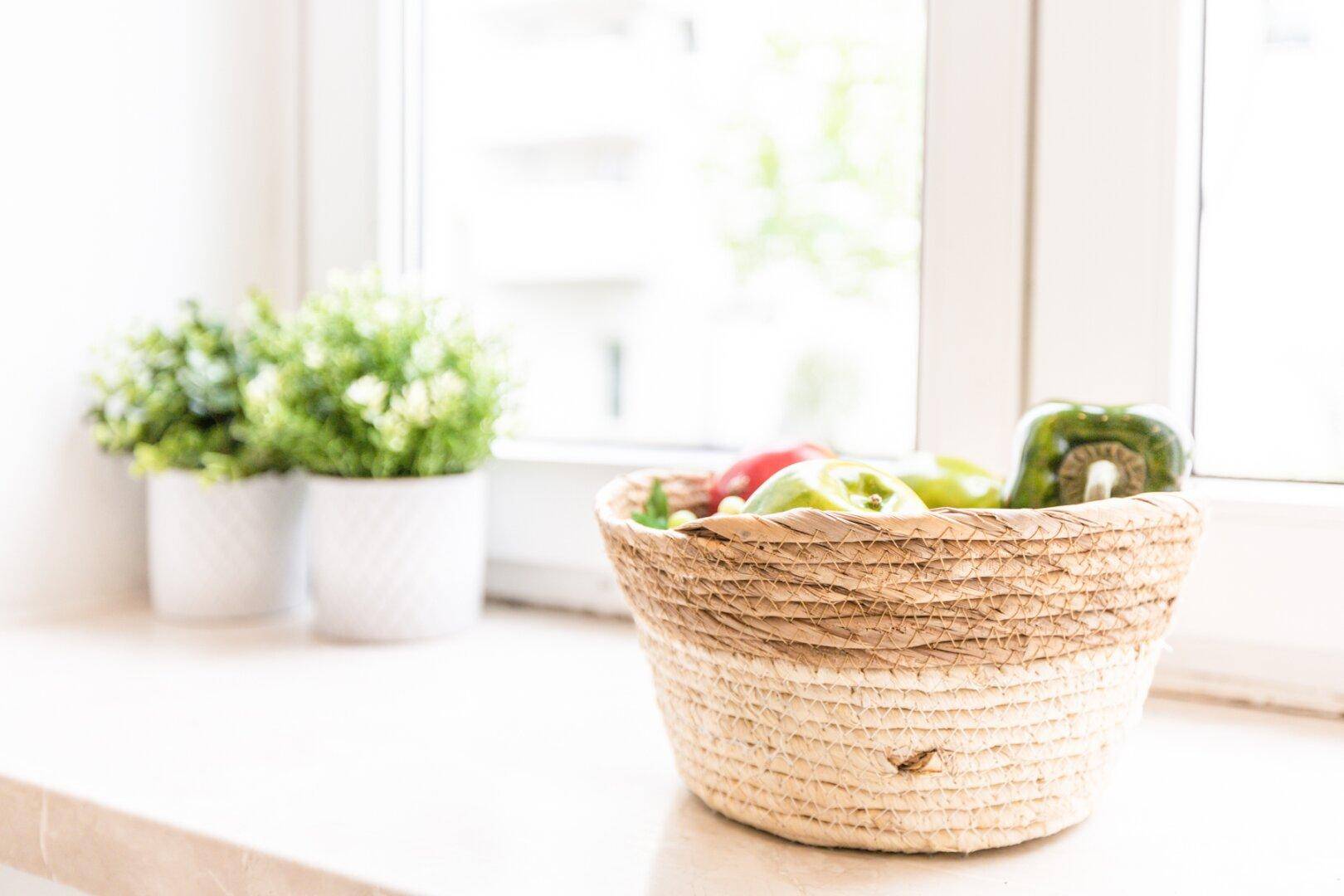 Nahaufnahme eines Korbes mit Obst und Topfpflanzen auf einer hellen Fensterbank.