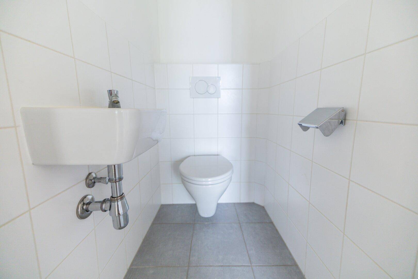 Kleines Gäste-WC mit weißen Fliesen, Toilette und einem kompakten Waschbecken.