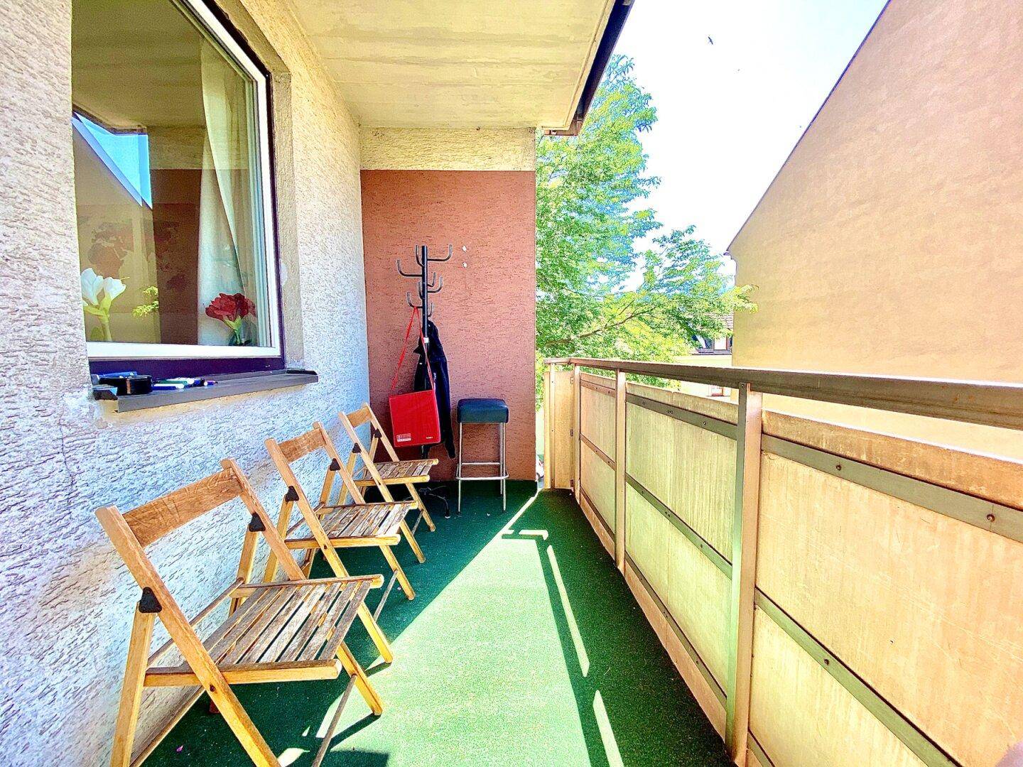 Möblierter Balkon mit grünem Teppichboden und Blick auf die grüne Umgebung.
