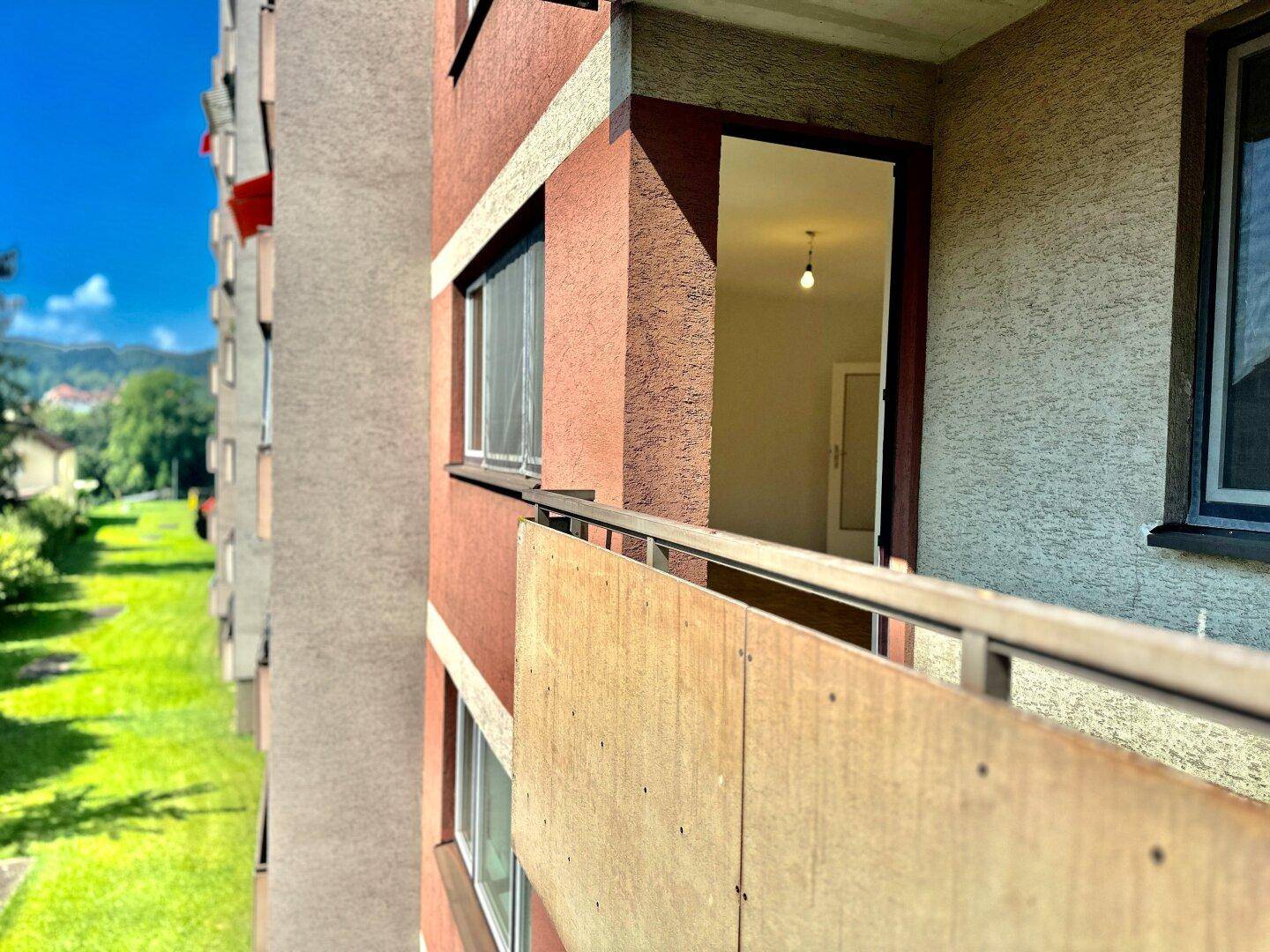 Blick vom Balkon auf die grüne Umgebung und die Fassade des Wohngebäudes bei Sonnenschein.