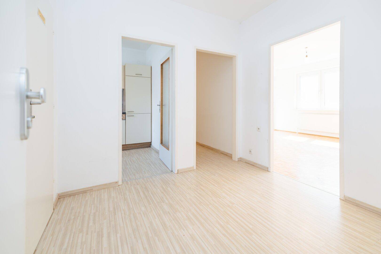 Heller Flur mit Laminatboden, der zu verschiedenen Zimmern und der Küche führt.
