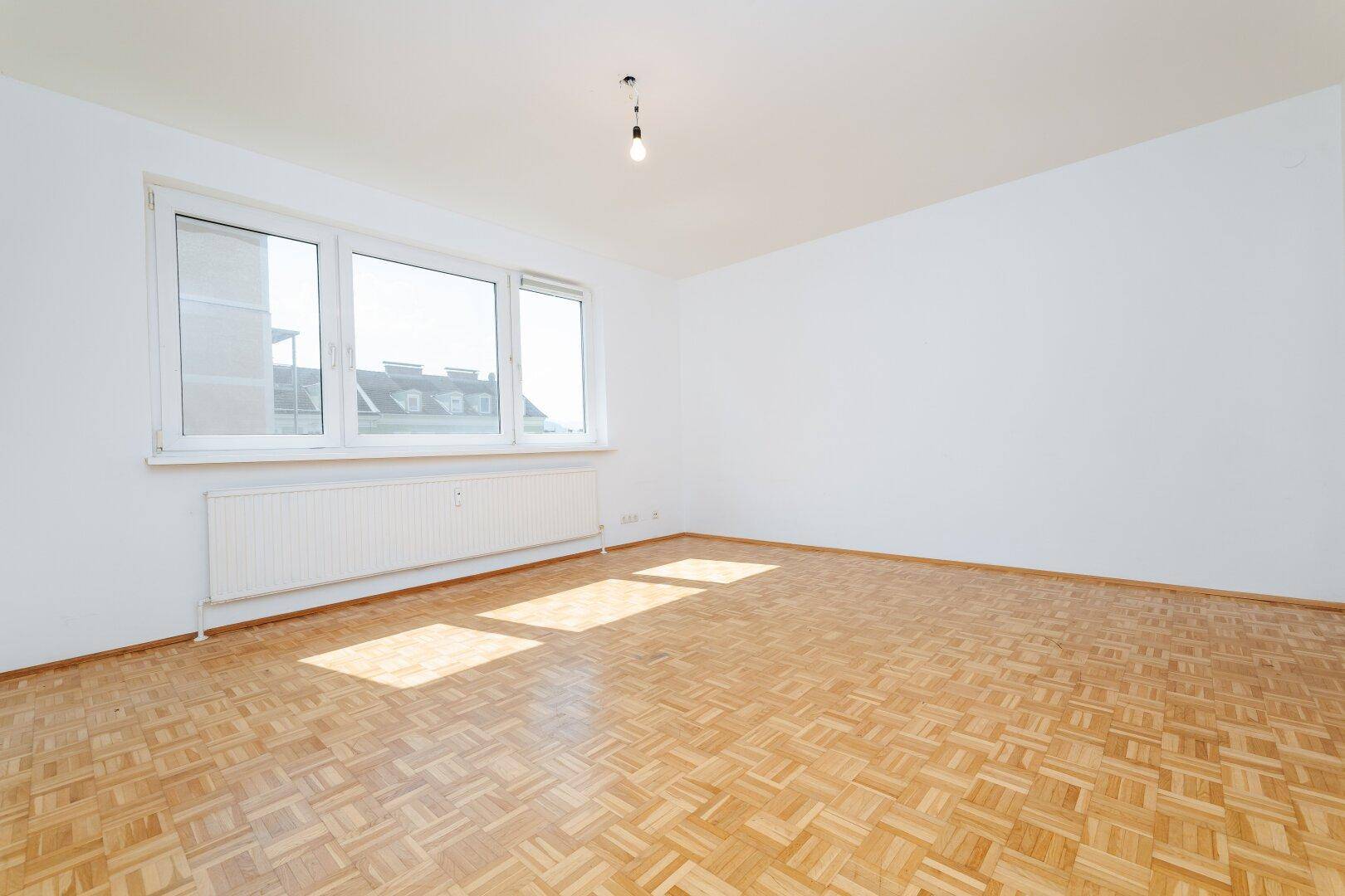 Großes, helles Wohnzimmer mit Parkettboden und breiter Fensterfront für viel Licht.