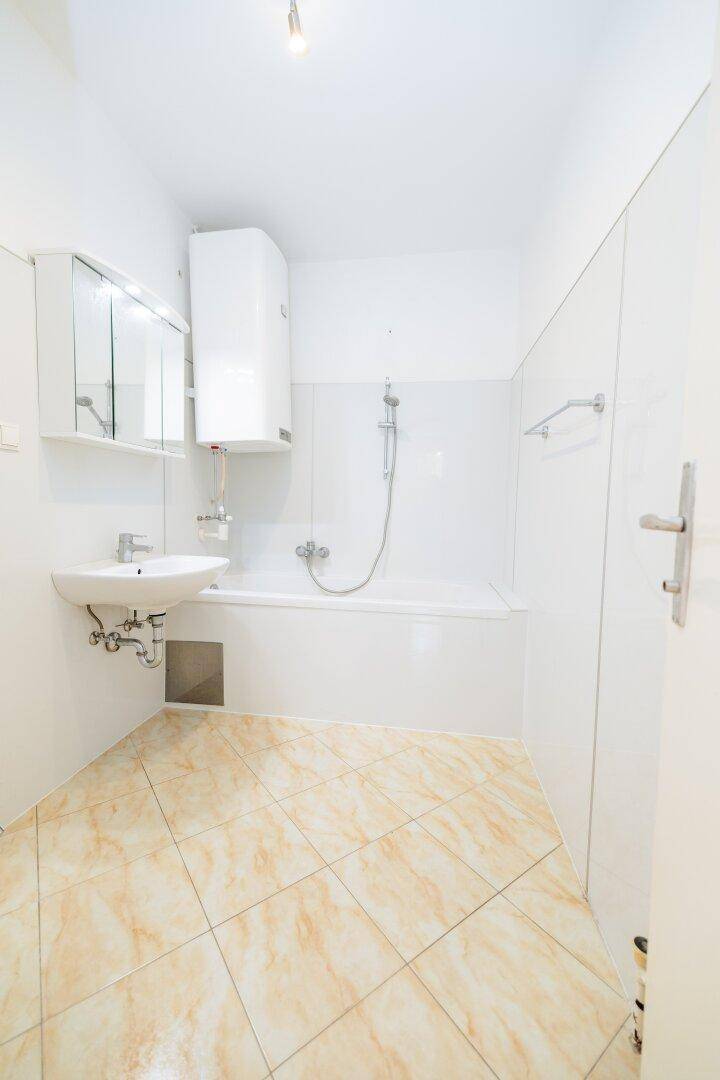 Helles Badezimmer mit Badewanne, Waschbecken und Fliesenboden in neutralen Farben.
