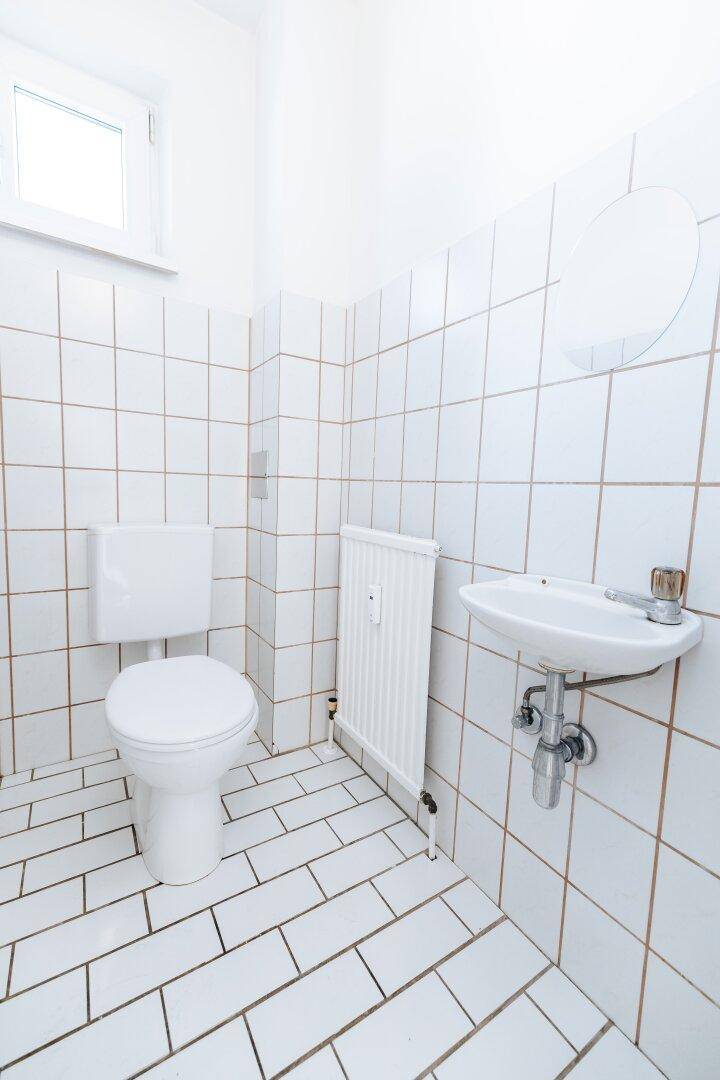Kleines, hell gefliestes WC mit Toilette, Waschbecken und Fenster für Tageslicht.