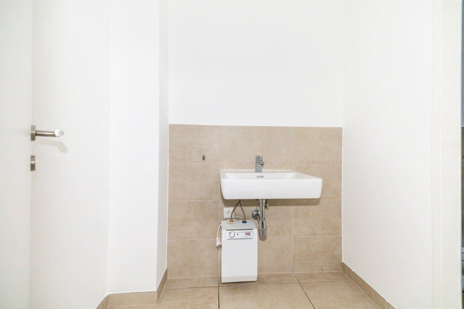 Nahaufnahme des Waschbeckens mit Untertischgerät in einem gefliesten Toilettenraum.