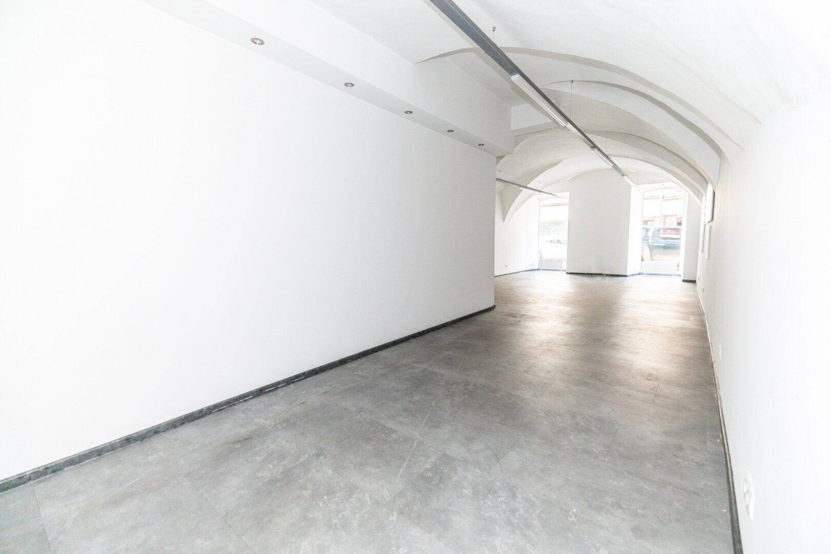 Langer, leerer Raum mit Gewölbedecken und Betonboden, ideal für gewerbliche Nutzung.