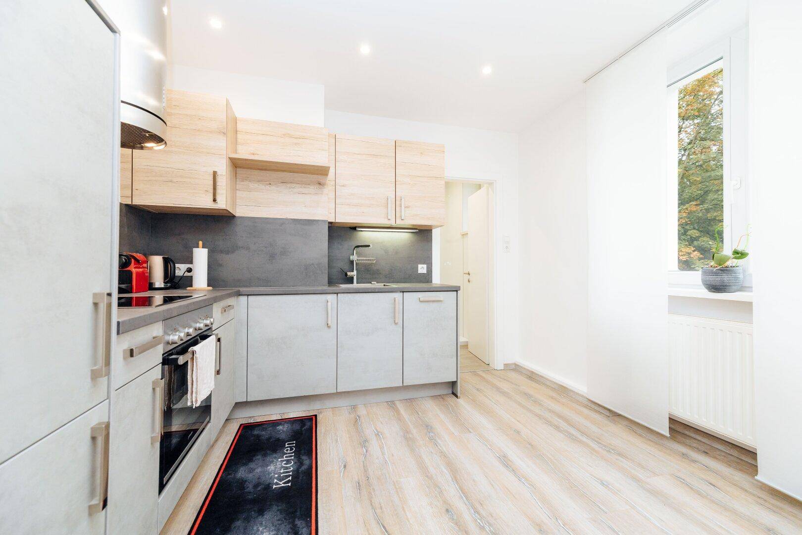 Funktionale Küche mit hellen Holz- und grauen Fronten, ausgestattet mit modernen Geräten und einem Fenster.