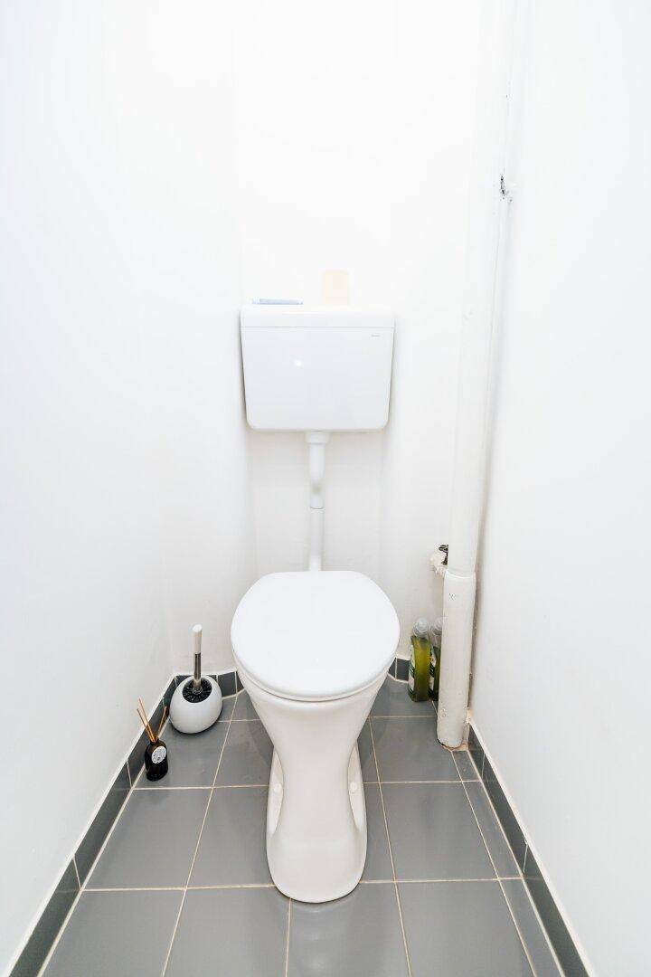 Kleines separates WC mit Toilette, grauen Bodenfliesen und weißen Wänden.