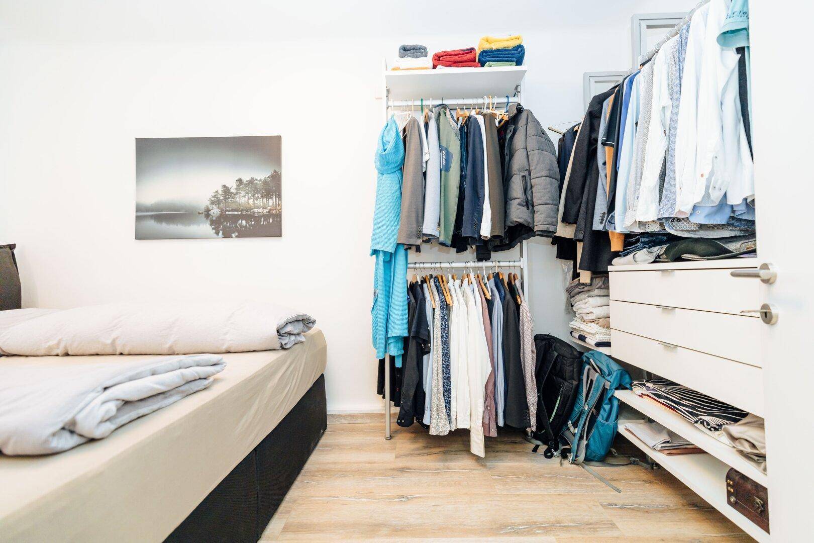 Schlafzimmer mit Bett, hellem Laminatboden und einem praktischen offenen Kleiderschranksystem.