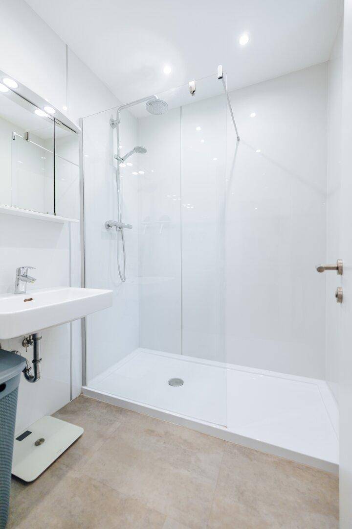 Modernes Badezimmer mit ebenerdiger Dusche, weiß gefliesten Wänden und einem einzelnen Waschbecken.