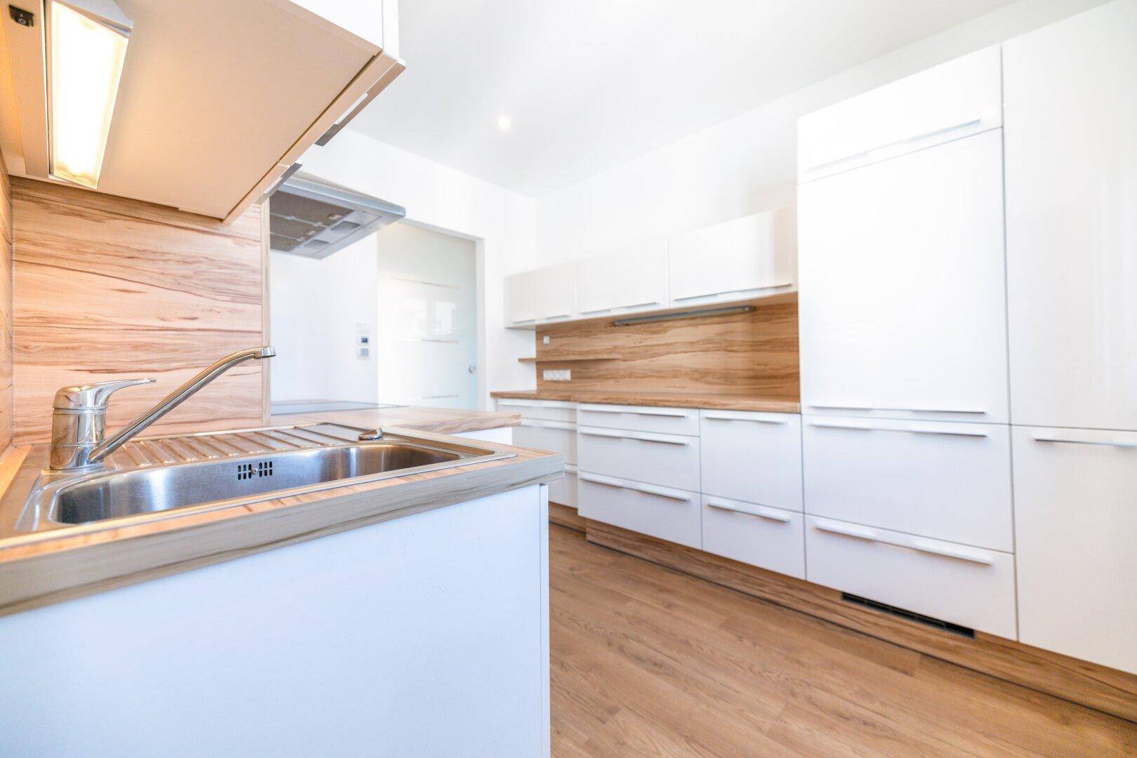 Helle Einbauküche mit weißen Fronten, Holzakzenten und integriertem Kühlschrank.