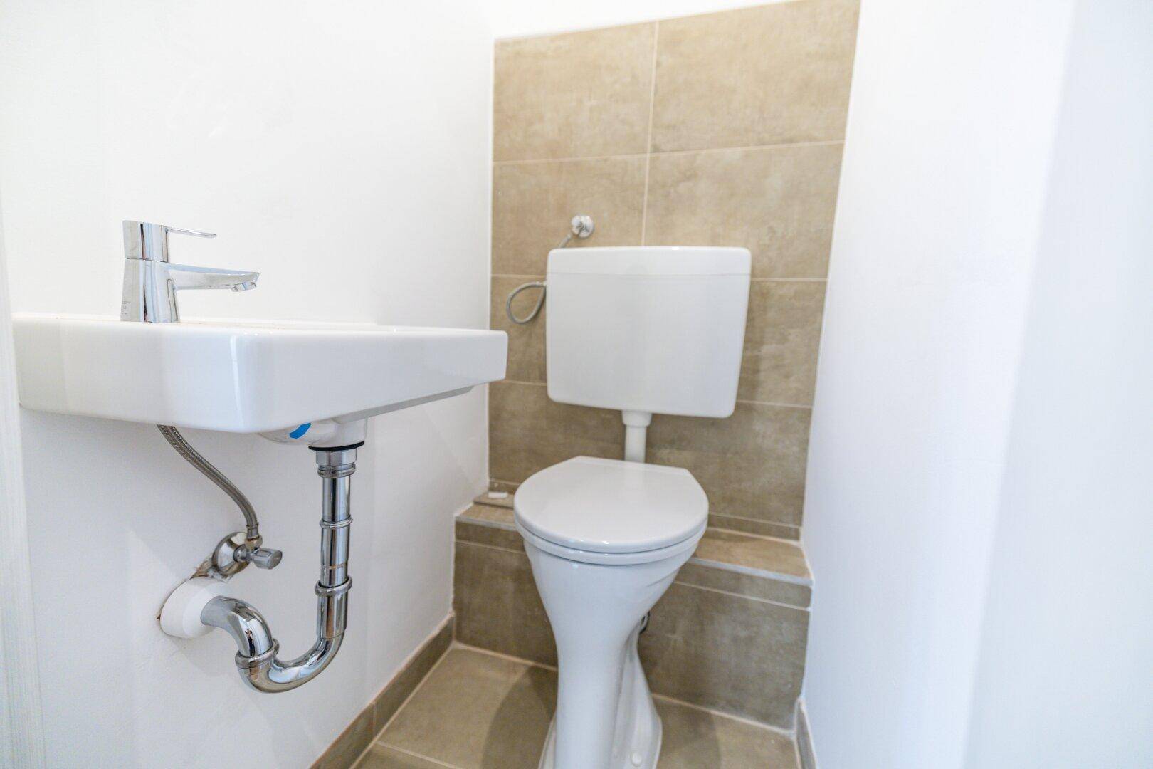 Kleines Gäste-WC mit Toilette und Waschbecken, ausgestattet mit beigefarbenen Fliesen.