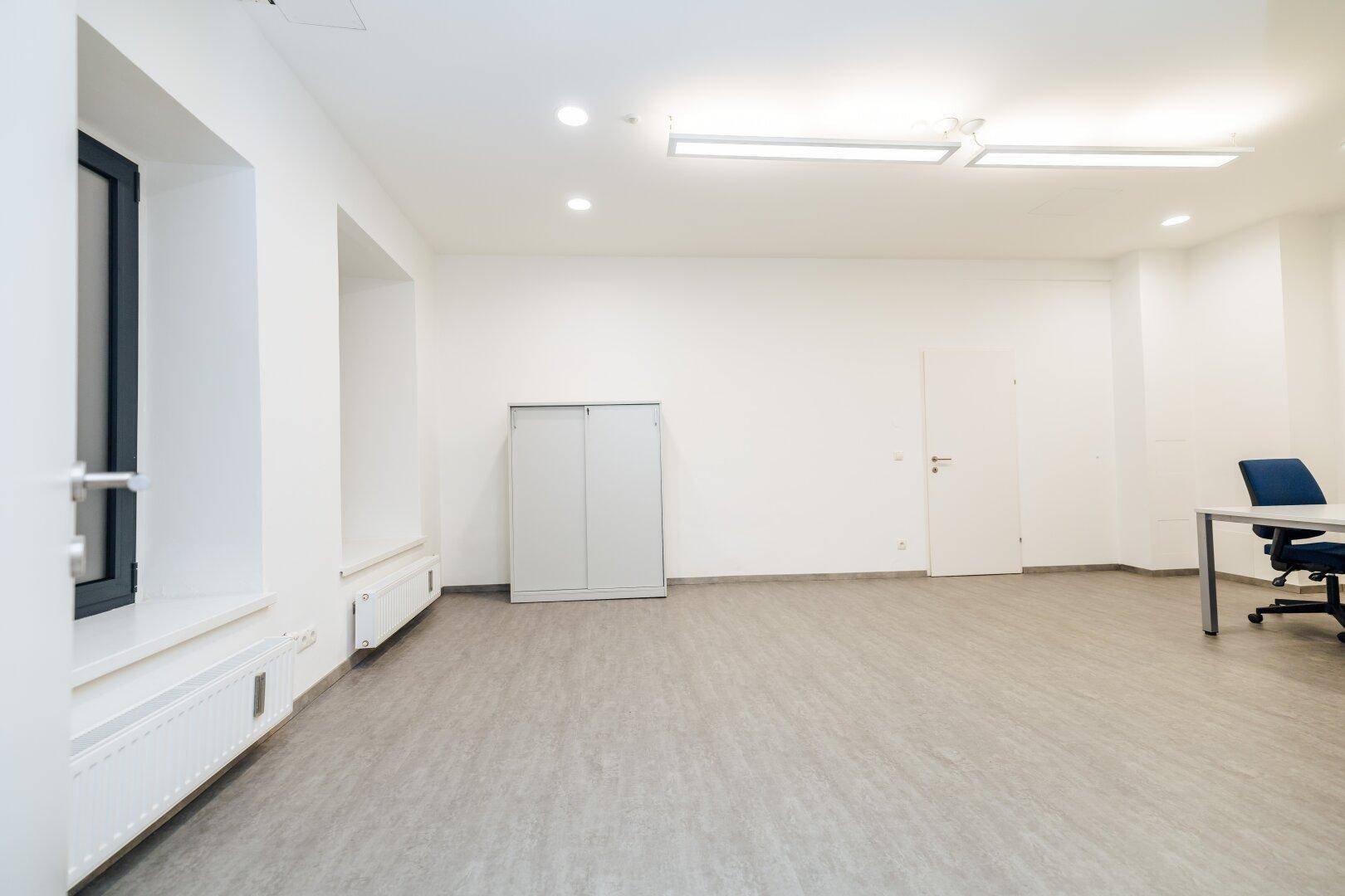Heller Büroraum mit Fenster, Einbauschrank und modernem Fliesenboden.