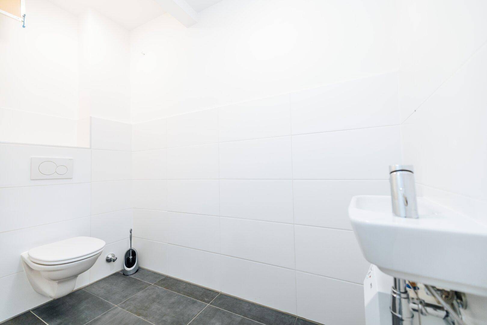Modernes Gäste-WC mit wandhängender Toilette, kleinem Waschbecken und dunklem Fliesenboden.
