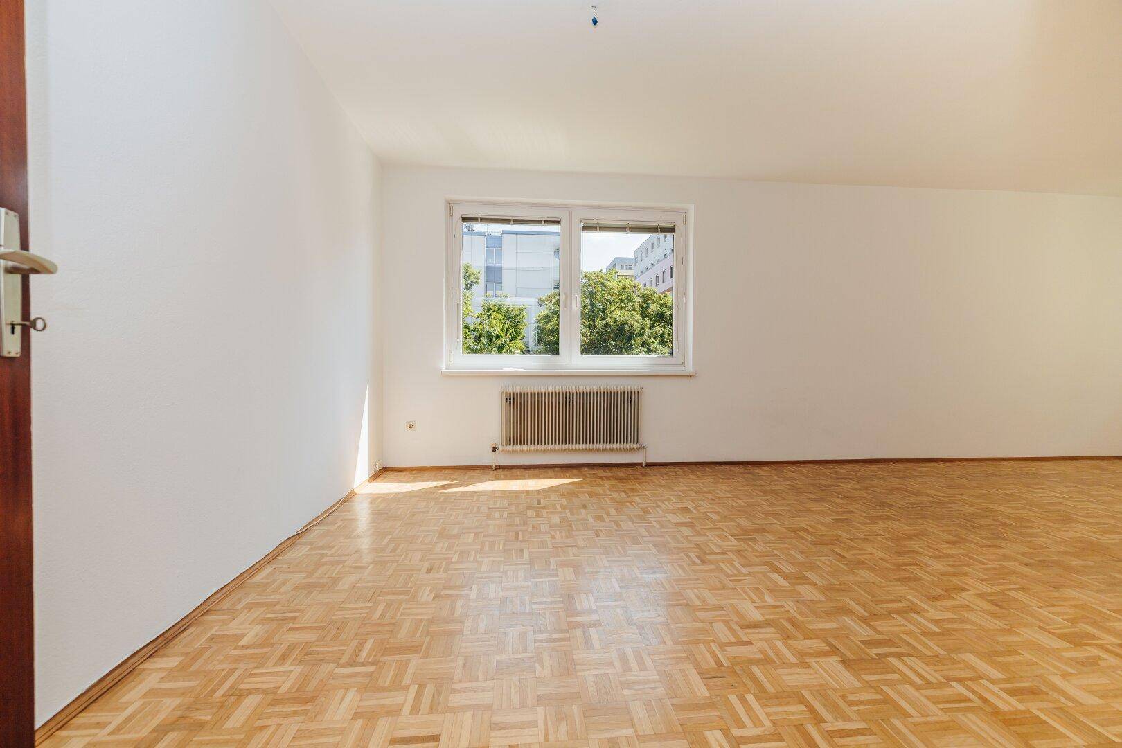 Geräumiges, helles Zimmer mit Parkettboden und Fenster mit Blick ins Grüne.
