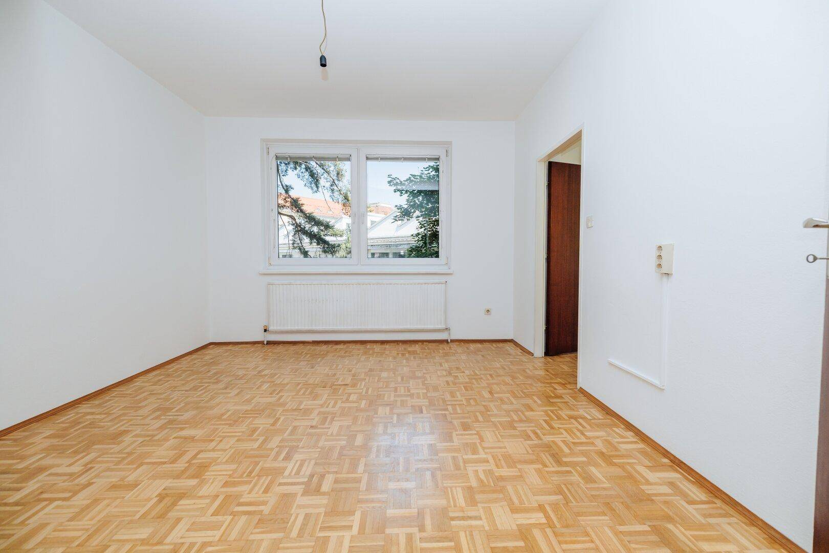 Helles Zimmer mit Parkettboden und offenem Zugang zu einem weiteren Raum.