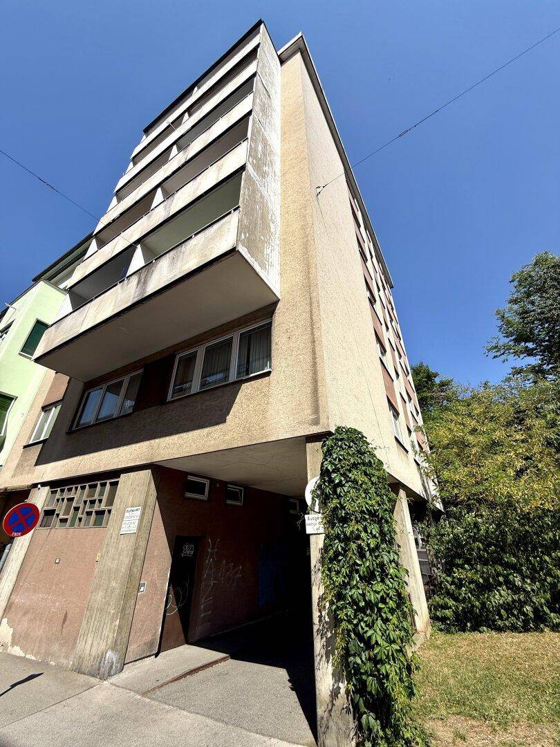 Mehrstöckiges Wohngebäude mit Balkonen und einer Fassade im Stil der 70er Jahre.
