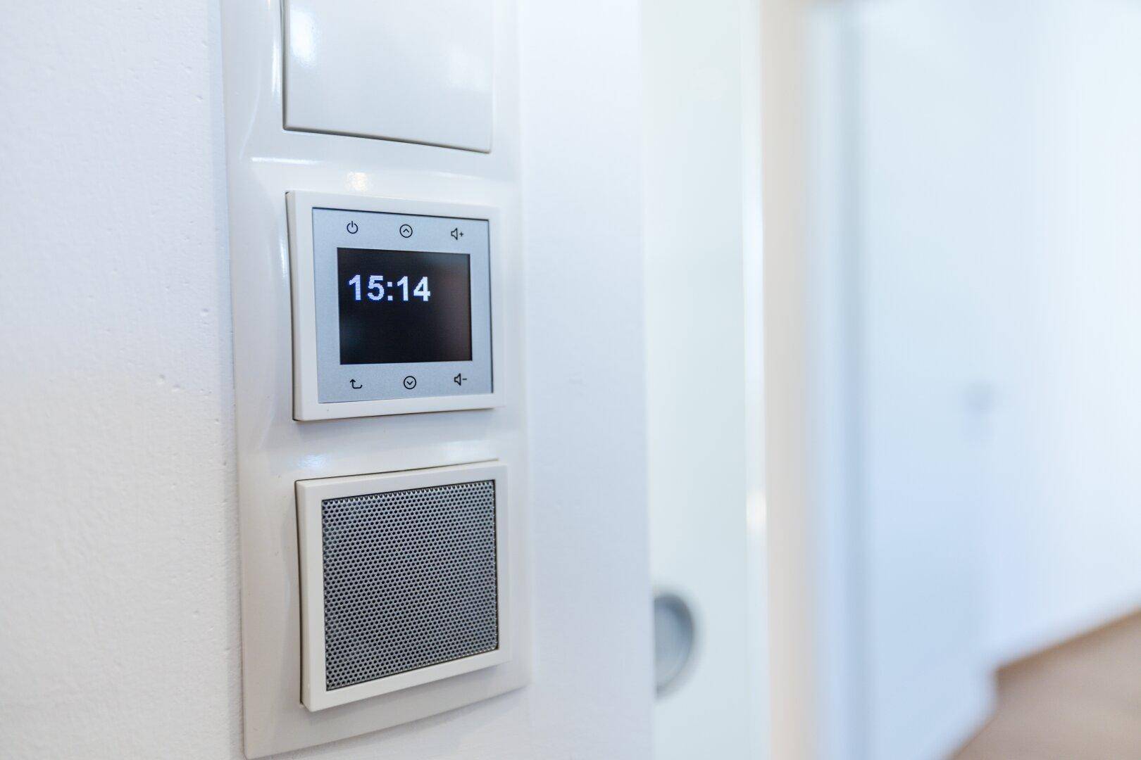 Nahaufnahme eines modernen Smart-Home-Bedienfelds mit digitaler Anzeige und integriertem Lautsprecher.