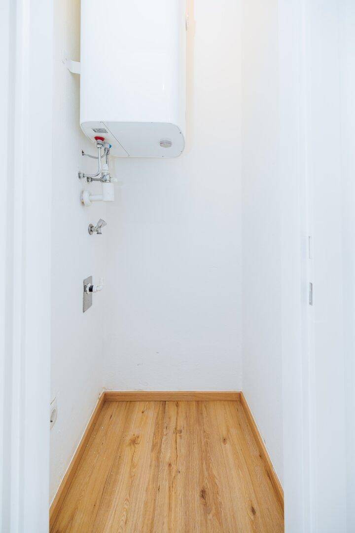 Kleiner Hauswirtschaftsraum mit Warmwasserbereiter und hellem Holzfußboden.