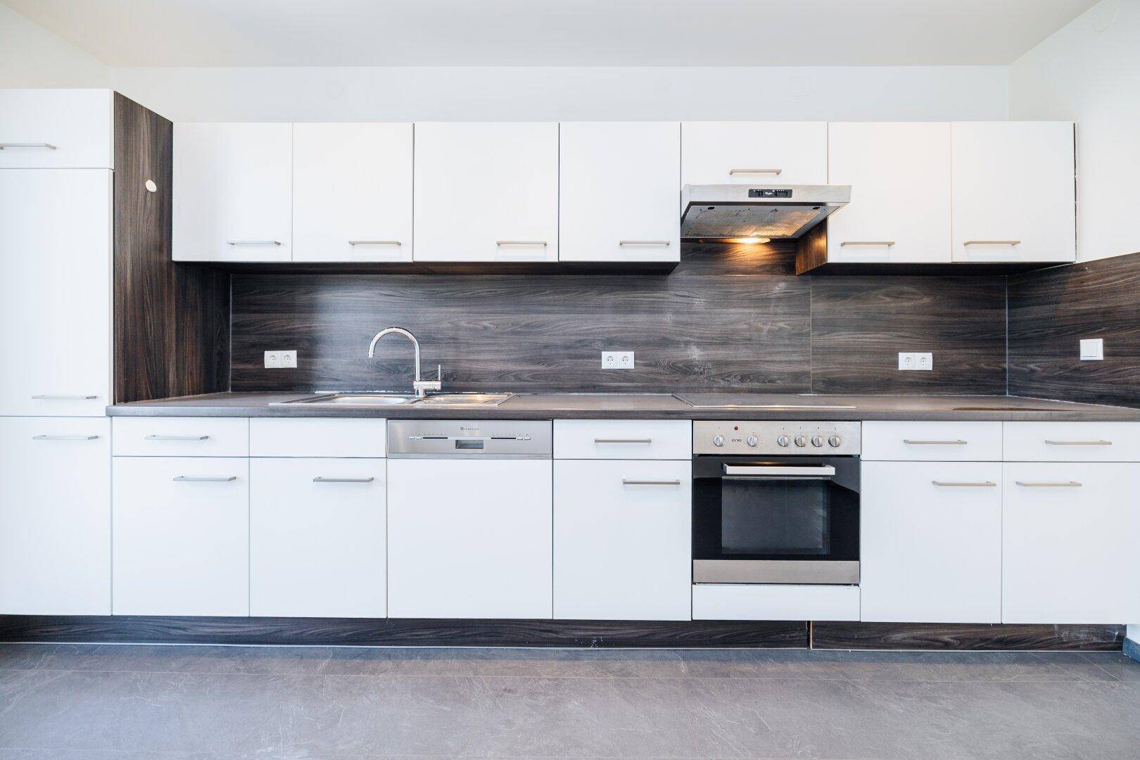 Moderne Einbauküche mit weißen Schränken, dunkler Arbeitsplatte und integrierten Geräten.