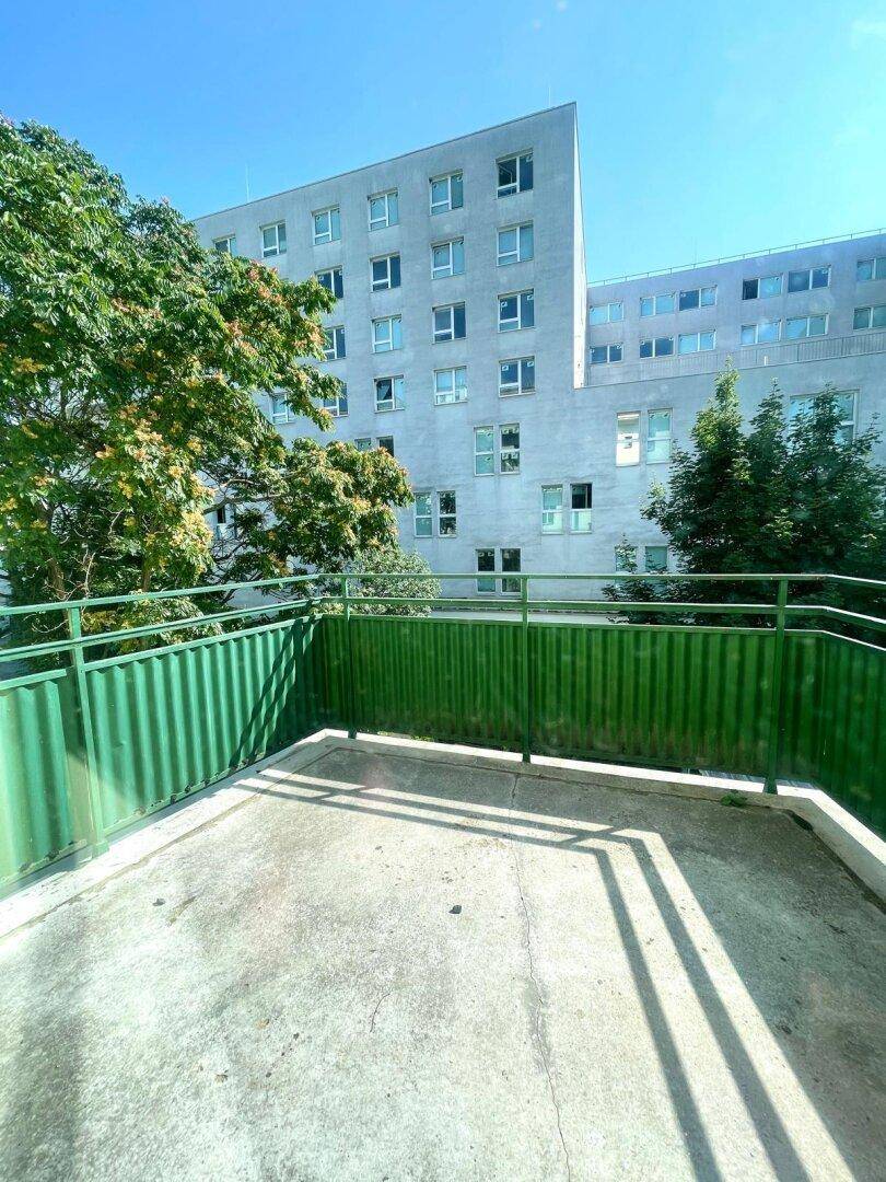 Betonbalkon mit grüner Brüstung und Blick auf die umliegenden Gebäude und Bäume.