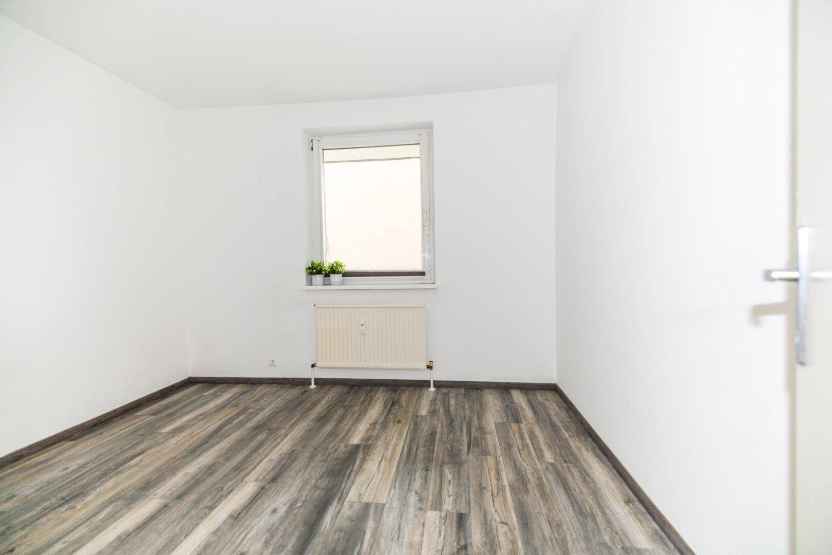 Helles Schlafzimmer mit Laminatboden, weißen Wänden und einem Fenster, bereit zur Einrichtung.
