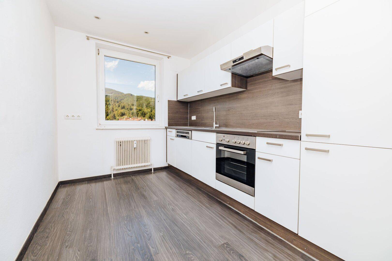 Moderne Einbauküche mit weißen Schränken, dunkler Arbeitsplatte und Fenster mit Blick ins Grüne.