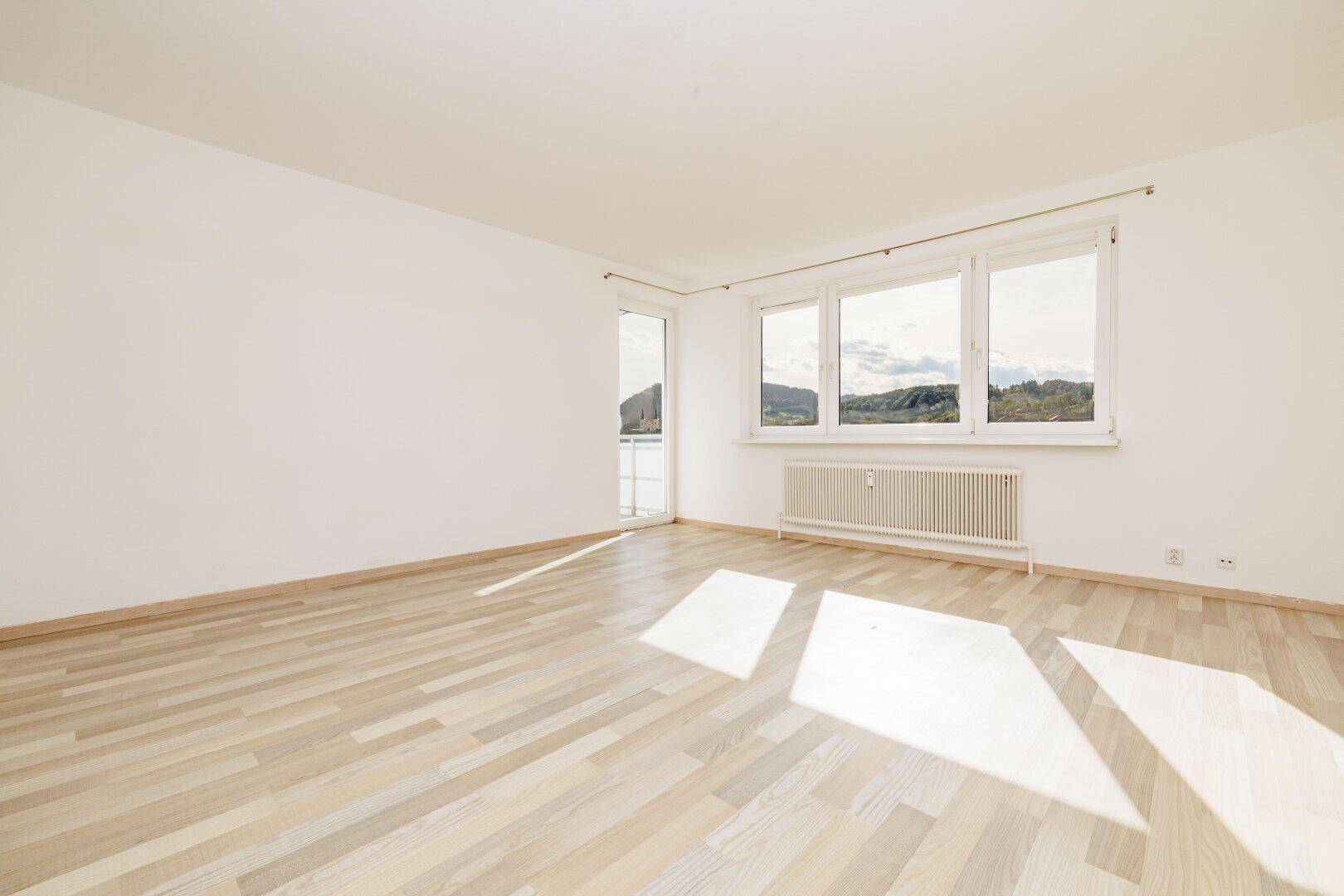 Heller Wohnraum mit hellem Laminatboden, großen Fenstern und Balkonzugang mit schöner Aussicht.
