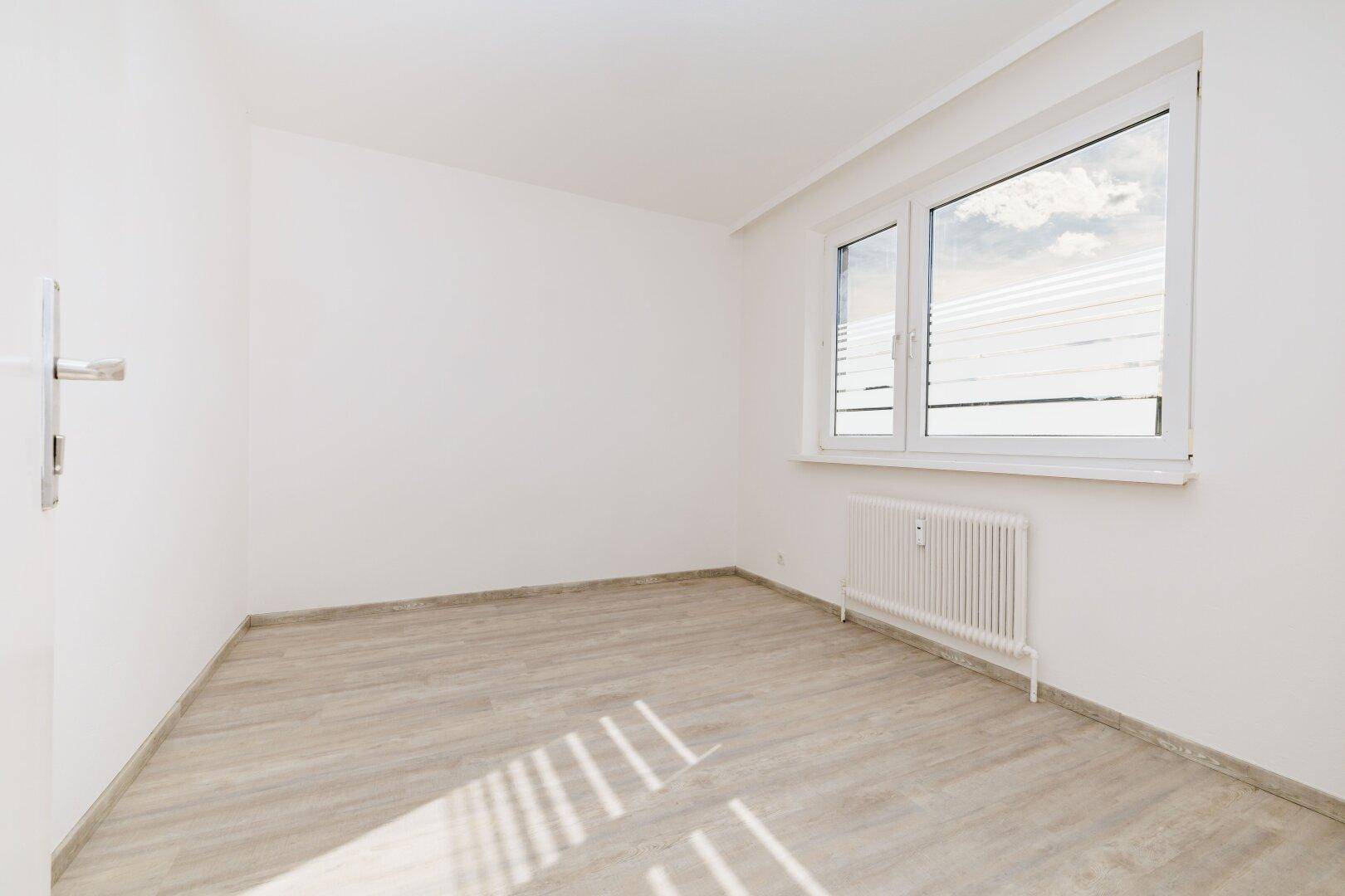 Geräumiges, helles Zimmer mit Laminatboden und einem großen Fenster für natürliche Belichtung.