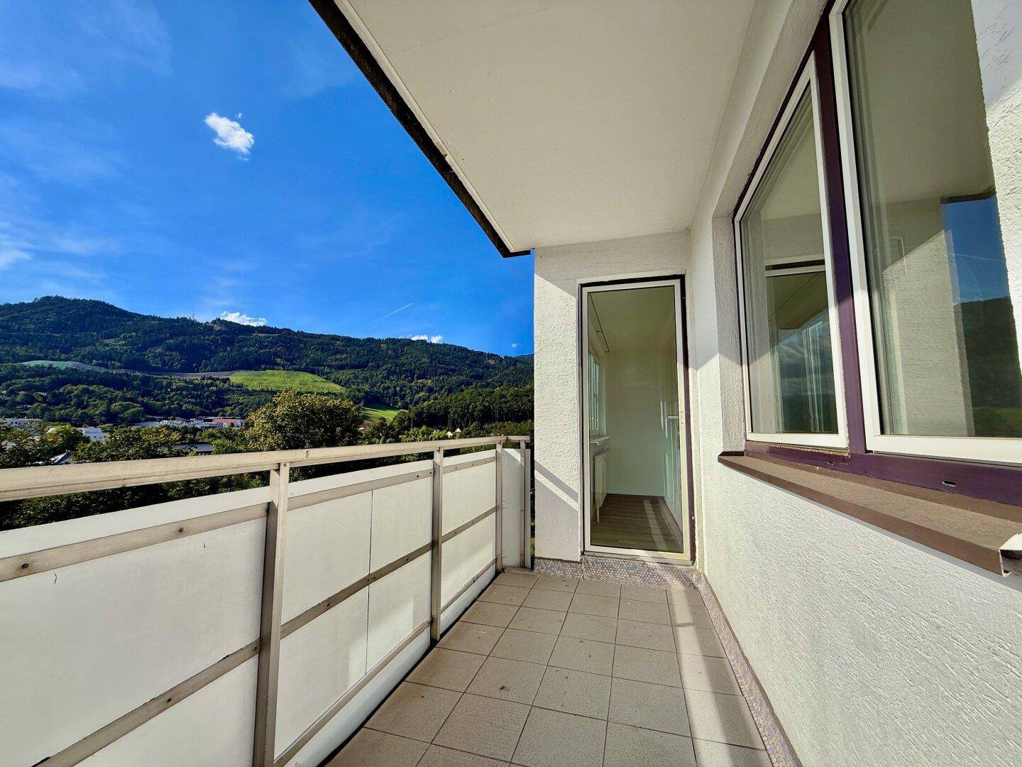 Sonniger Balkon mit Fliesenboden und weitem Blick auf die grünen Hügel und die Berglandschaft.