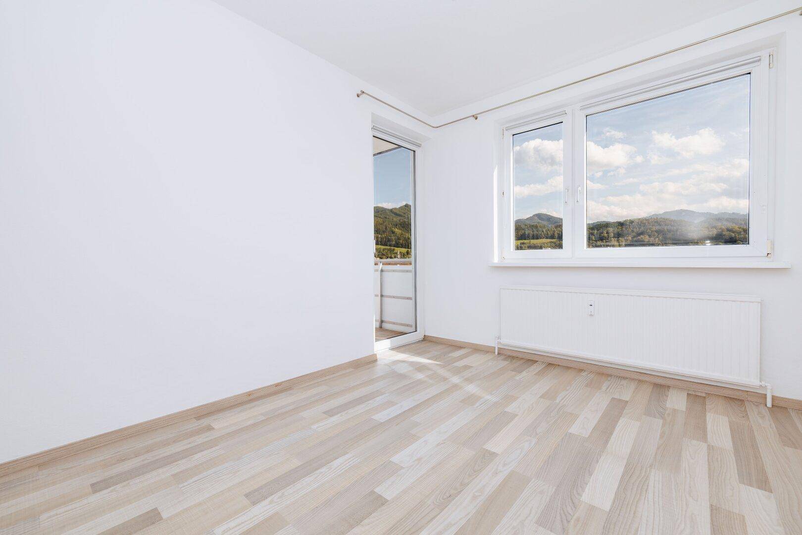 Lichtdurchfluteter Wohnraum mit hellem Laminatboden und Zugang zu einem Balkon mit schöner Aussicht.