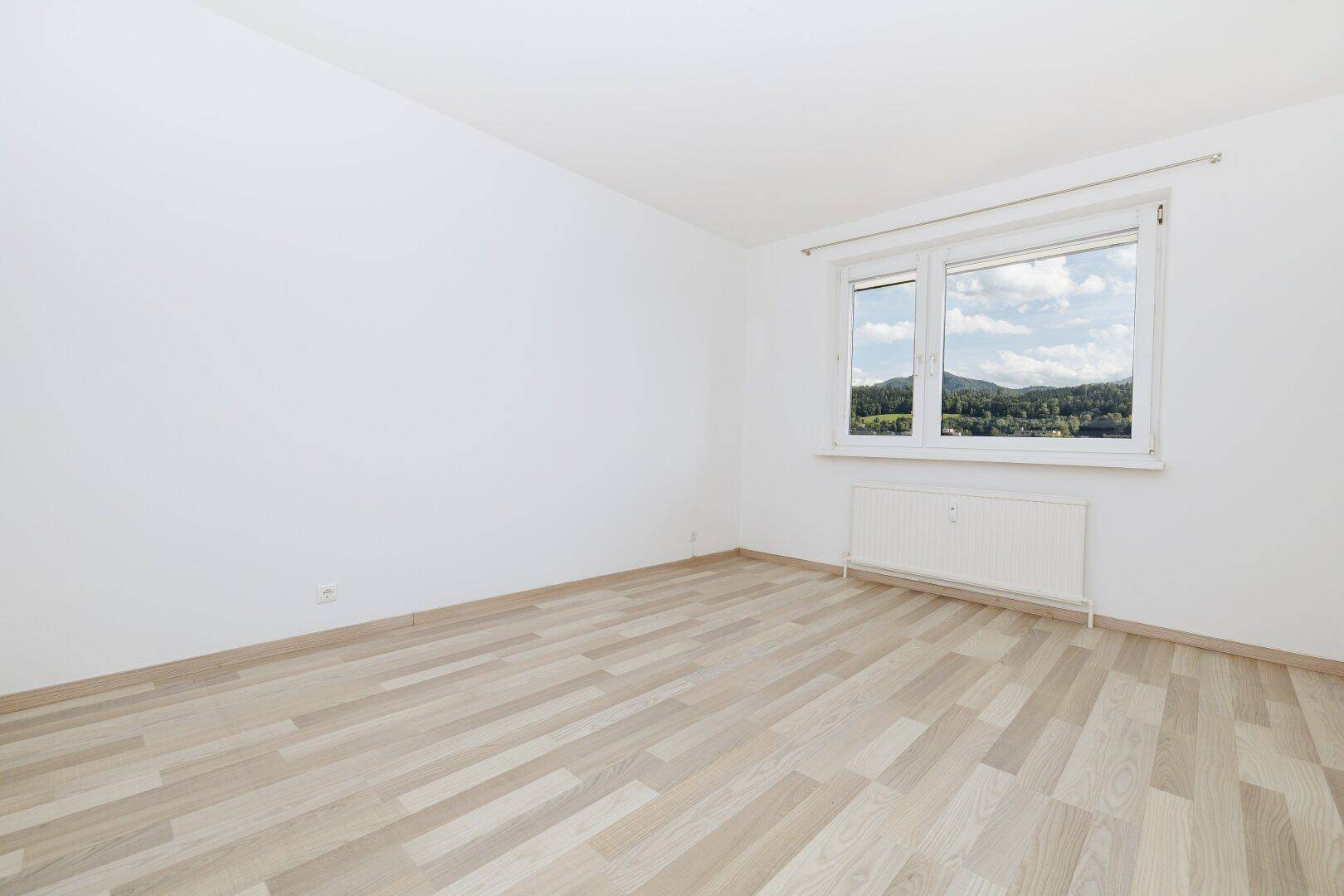 Helles Zimmer mit Laminatboden und Fenster, das einen schönen Blick ins Grüne bietet.