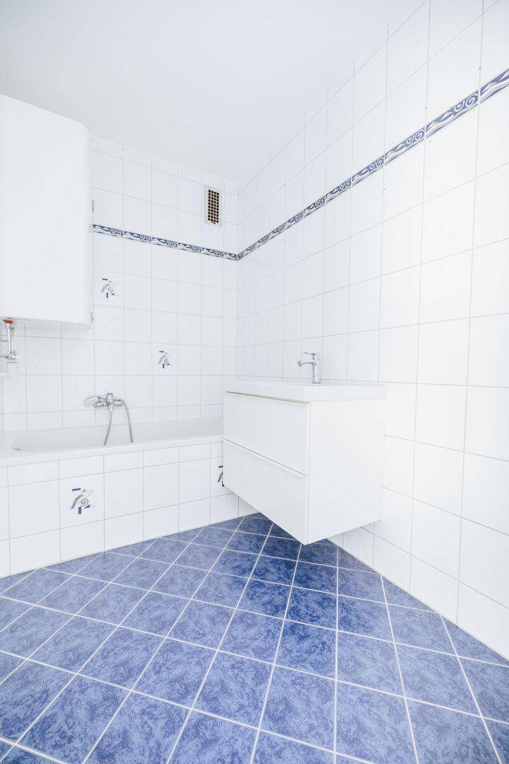 Badezimmer mit weiß-blauen Fliesen, Badewanne, schwebendem Waschtisch und Abluftventilator.