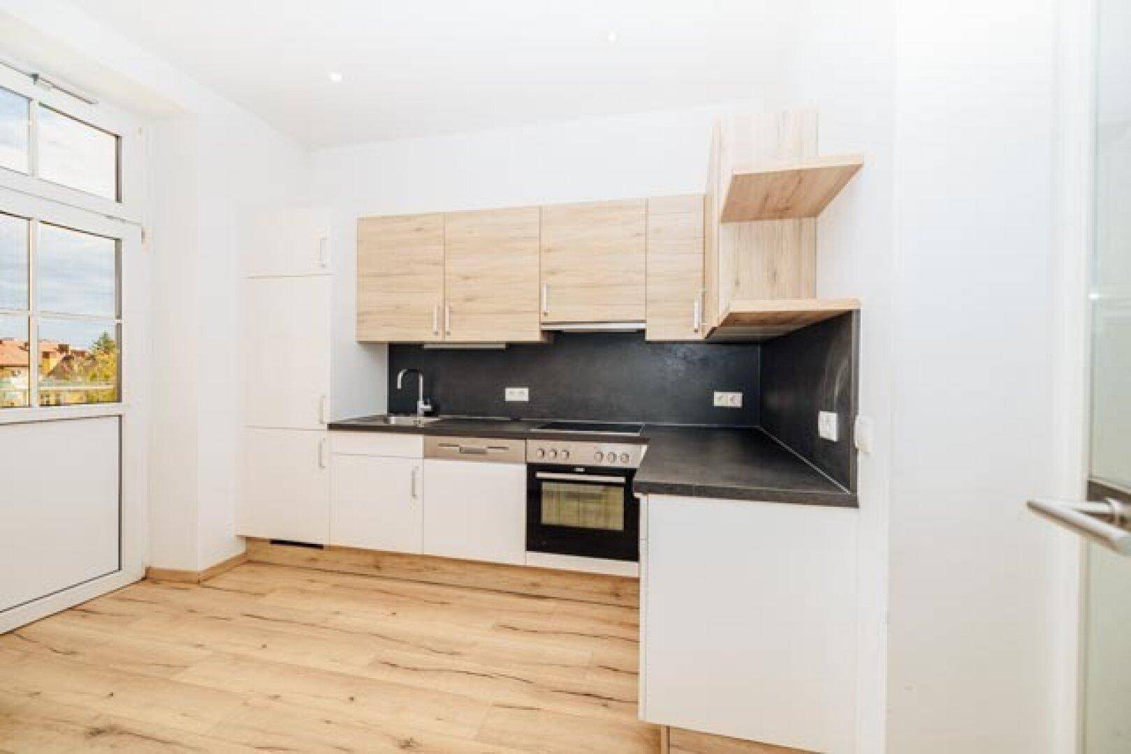 Moderne Einbauküche mit hellen Holz- und weißen Fronten, schwarzer Arbeitsplatte und Zugang nach draußen.