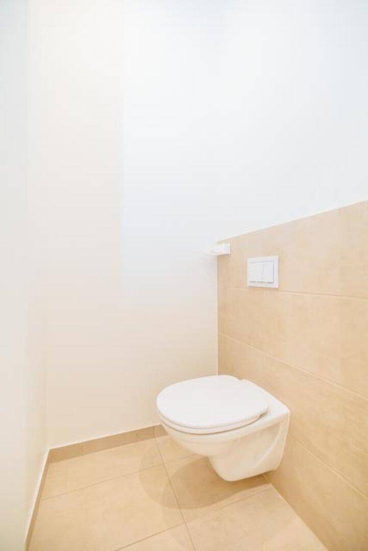 Separates WC mit wandhängender Toilette und beigefarbenen Fliesen an Wänden und Boden.