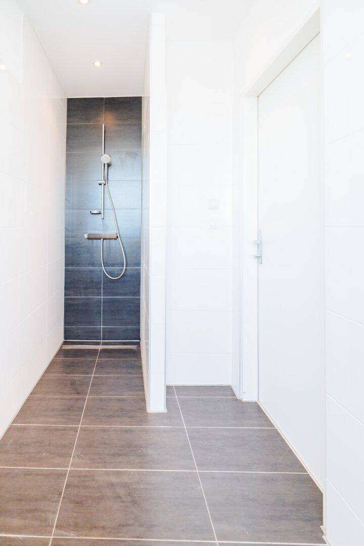 Geräumige begehbare Dusche mit dunklen Wandfliesen und hellem Boden in modernem Badezimmer.