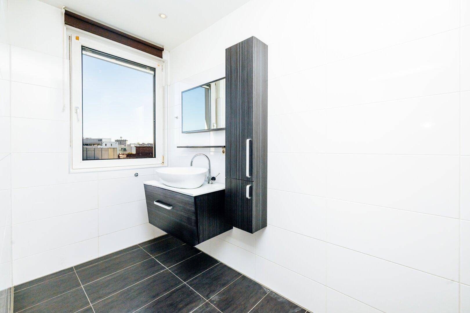 Modernes Badezimmer mit schwebendem Waschtisch, dunklen Bodenfliesen und einem Fenster.